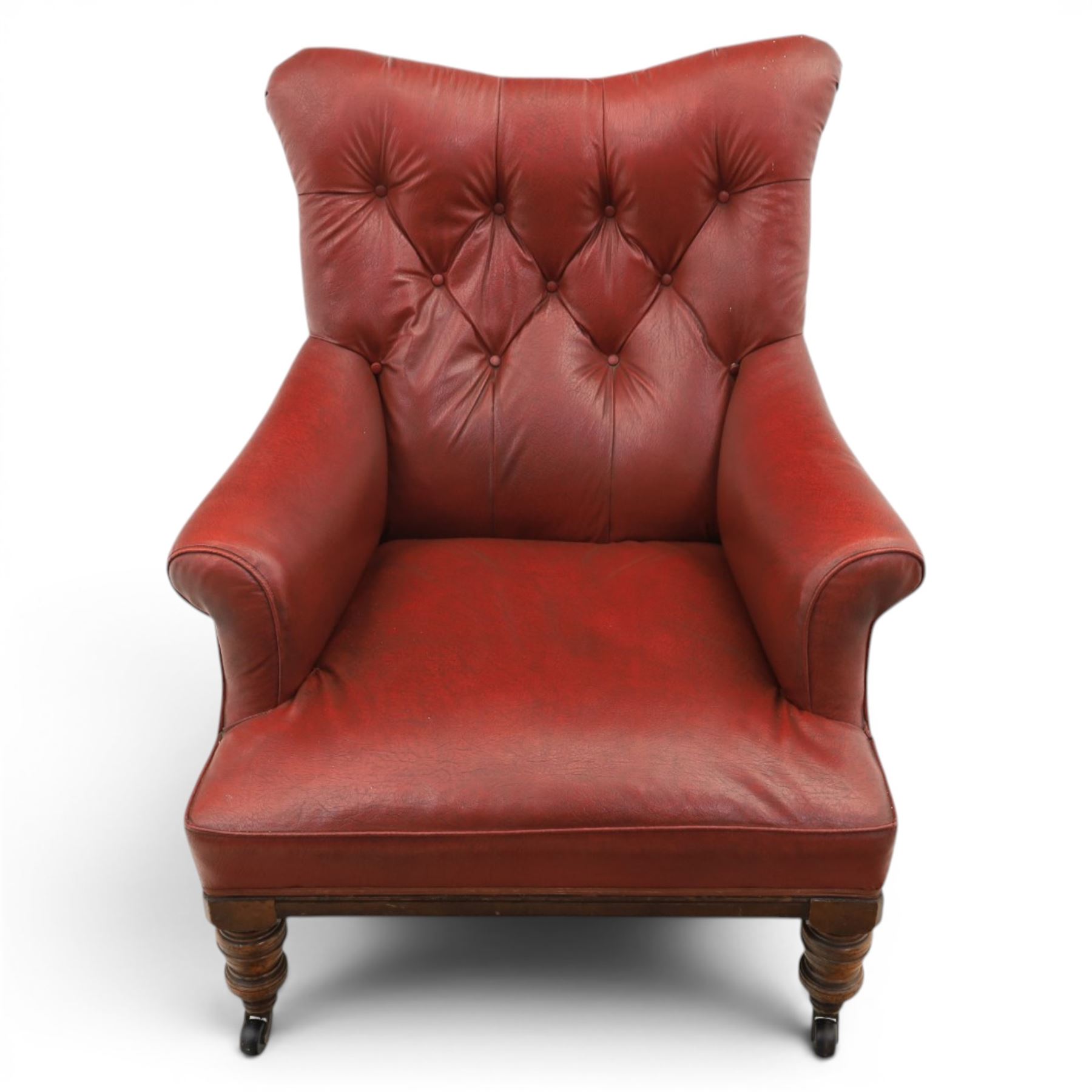Early 20th century style oxblood red leather Chesterfield armchair, deep buttoned shaped back over padded scroll arms and loose seat cushion, raised on turned mahogany front supports with brass caps and castors