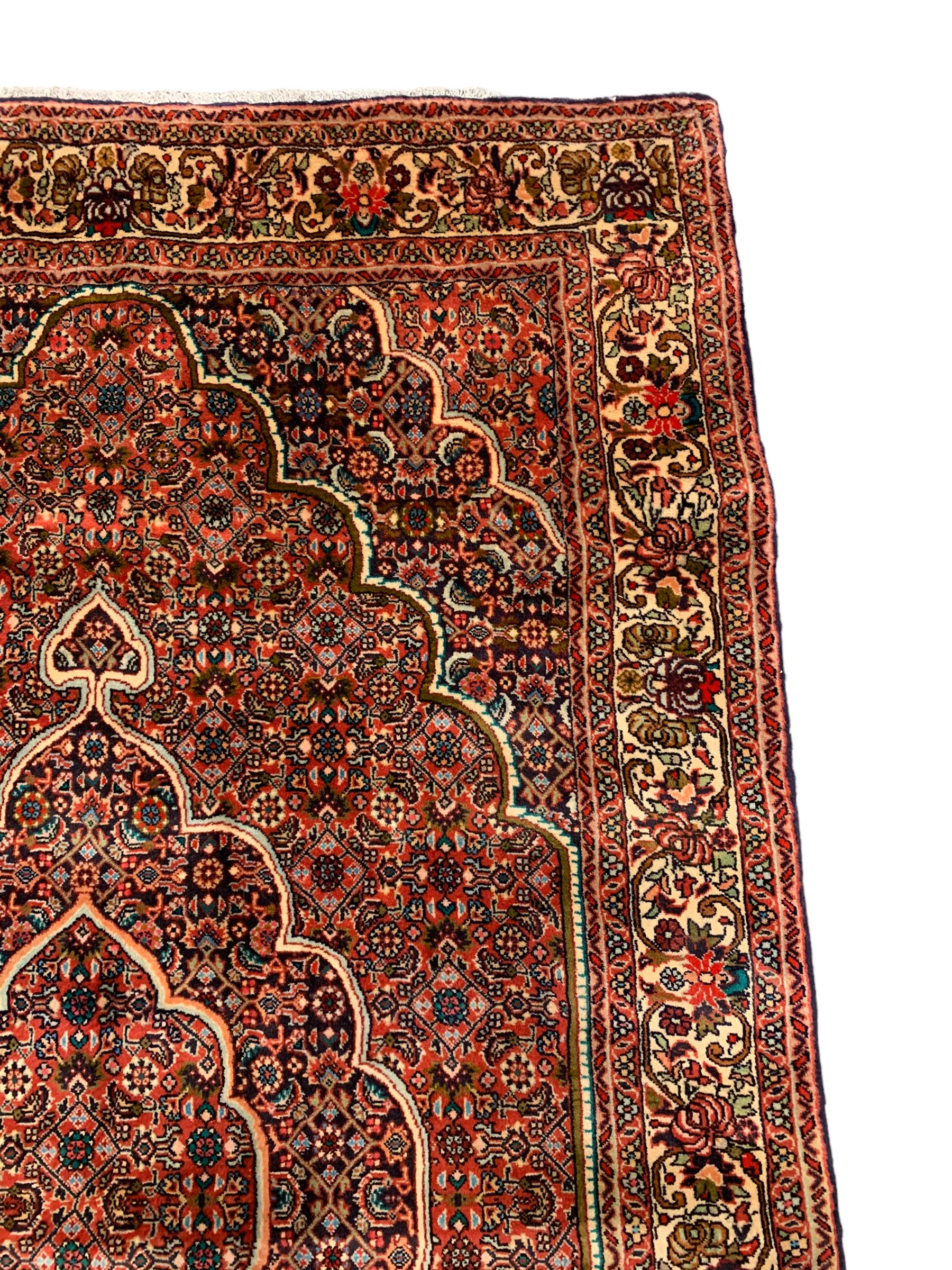 Persian Bidjar crimson ground rug, thick woollen pile, the field decorated with repeating Herati motifs within cusped outlines, the guarded border decorated with repeating flower head motifs