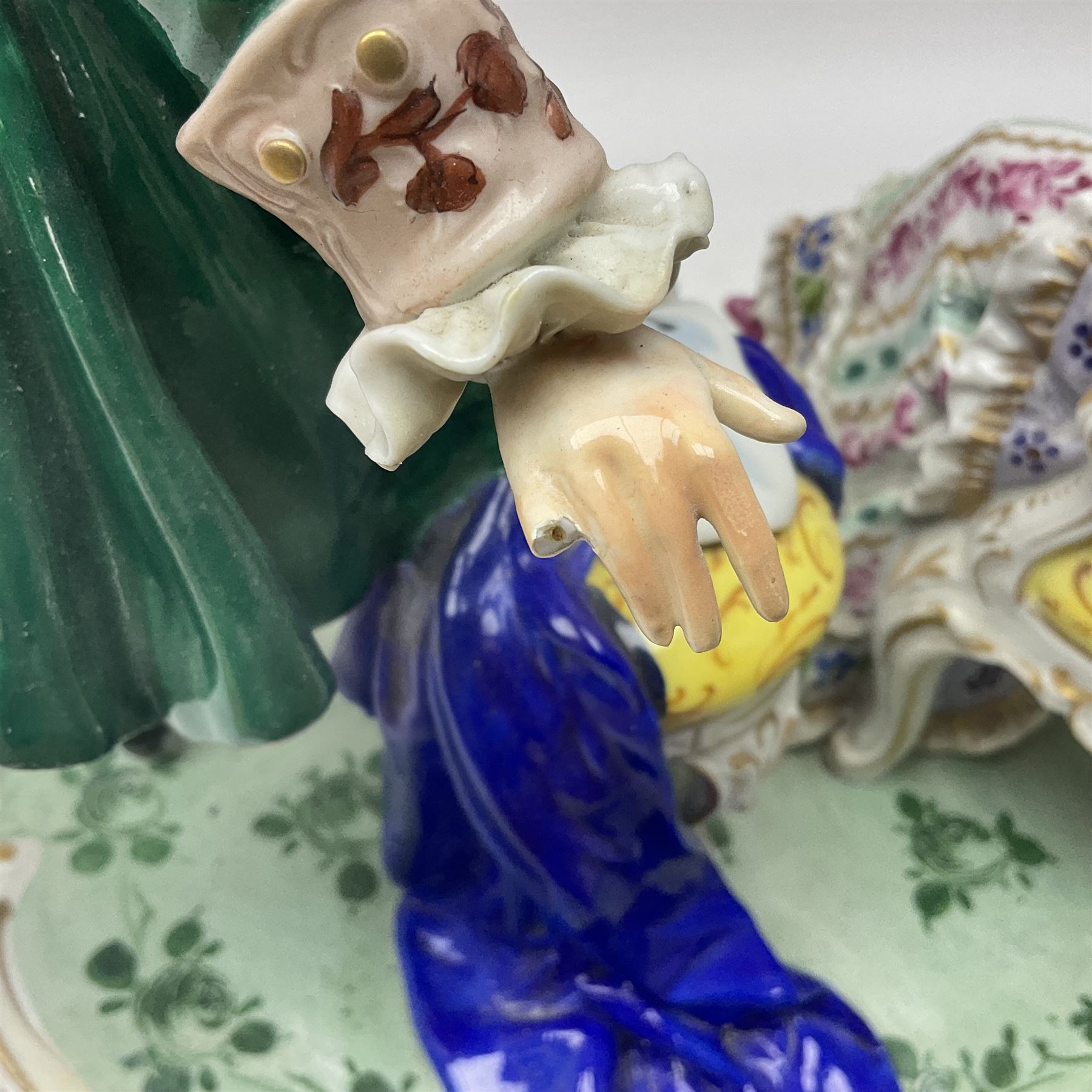 20th century Naples figure group, modelled as a seated female figure playing the lute seated, before a male figure stood holding a sheet of music, each in period dress, upon an oval base with gilt heightened scroll edge, with crowned N mark beneath, H31.5cm L33cm
