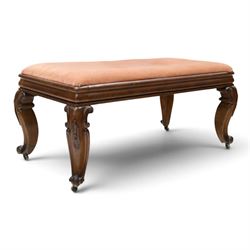 Victorian carved mahogany fender stool of generous proportions, the wide rectangular seat upholstered in rose fabric, shaped frieze rail over C-scroll and cartouche carved cabriole supports with scroll feet and brass castors