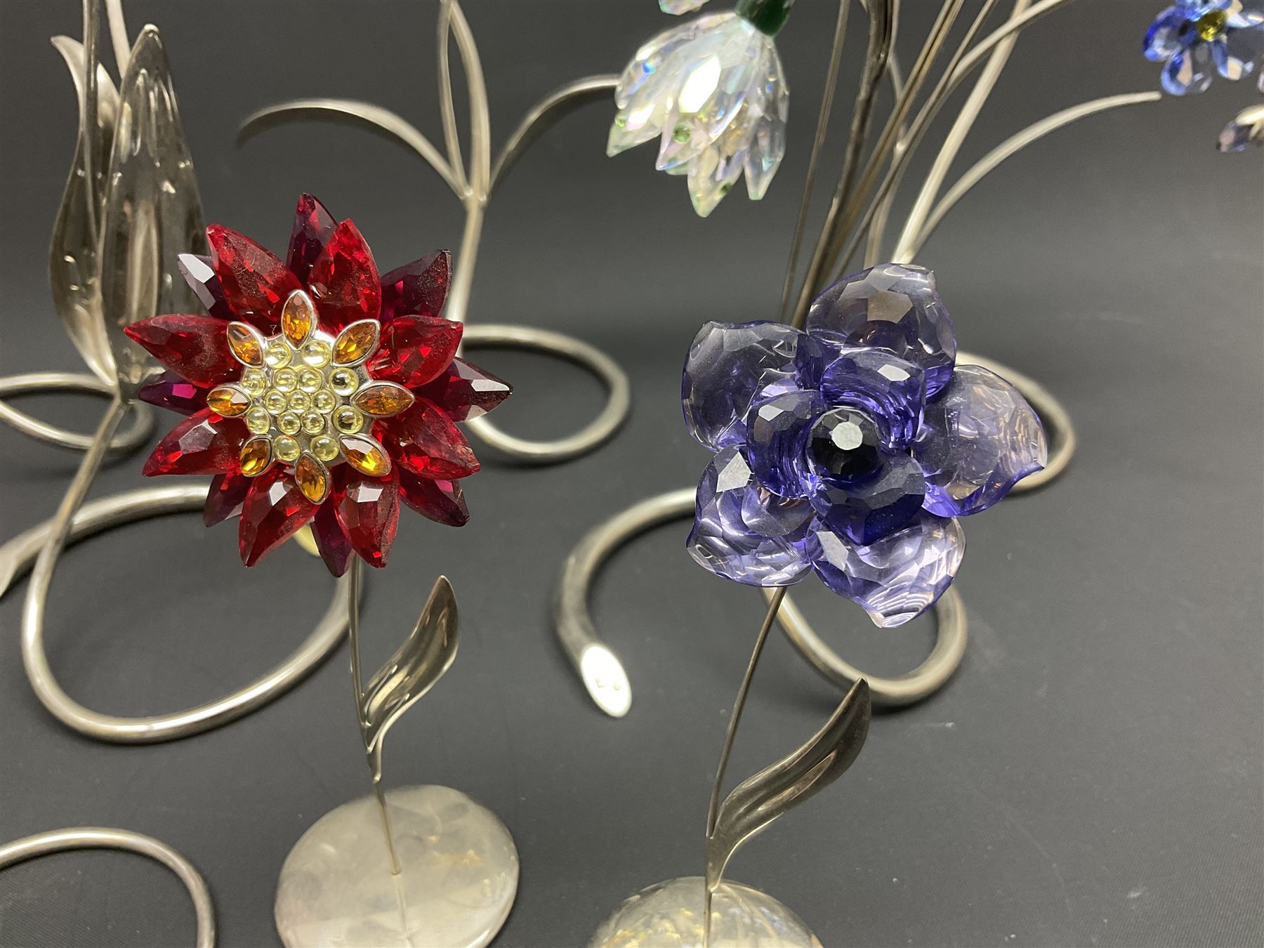 Eleven Swarovski Crystal flowers, to include violet, sunflower, delphinium, forget-me-not and lily-of-the-valley, each on stylised metal stems, tallest H23cm