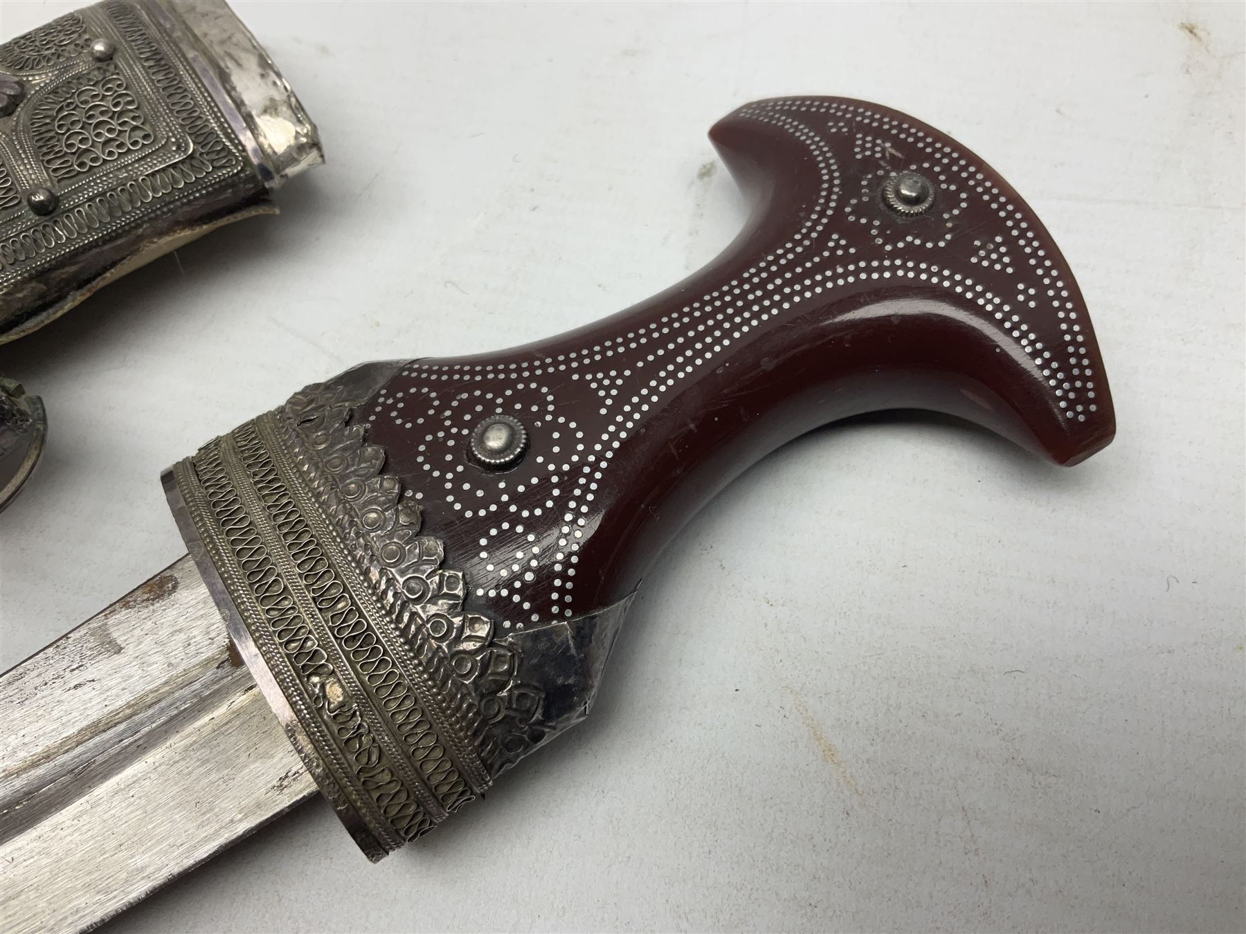 Omani Khanjar dagger, the 12.5cm curved blade with pronounced medial rib to either side, waisted horn style hilt with dome shaped pommel and inlaid pique work; in an intricately filigree decorated white metal scabbard with rings woven into the belt mount L25cm overall