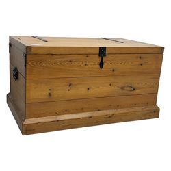 Contemporary polished pine blanket chest, the hinged planked lid with iron strap hinges and clasp fitting, plain boarded sides, fitted with blackened metal drop handles, on a moulded plinth base