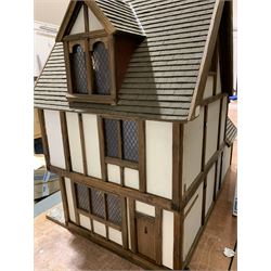 Gerry Welch for Manorcraft Tudor style wooden doll's house, of three-storey multi gabled form with mock beam and plaster walls and simulated leaded glass windows under a felt tiled roof, boarded floors and stairs to each room, curtains to most windows, front entrance door, rear door and single storey extension for kitchen. Furniture includes fitted floral bathroom suite to top floor, well stocked Welsh dresser with copperware etc, tapestry style wall hangings, knole settee, tin bath, metal range, fire-surround, wooden three-piece suite etc; on shaped cobbled base W91cm D61cm H91cm