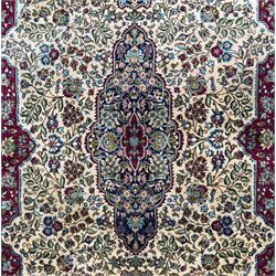 Central Persian Ghom hand-knotted rug, ivory field with scrolling vines, palmettes and flowerheads around a central lobbed medallion with pendants, framed by burgundy spandrels and a navy border of rosettes and arabesques, 289cm x 214cm