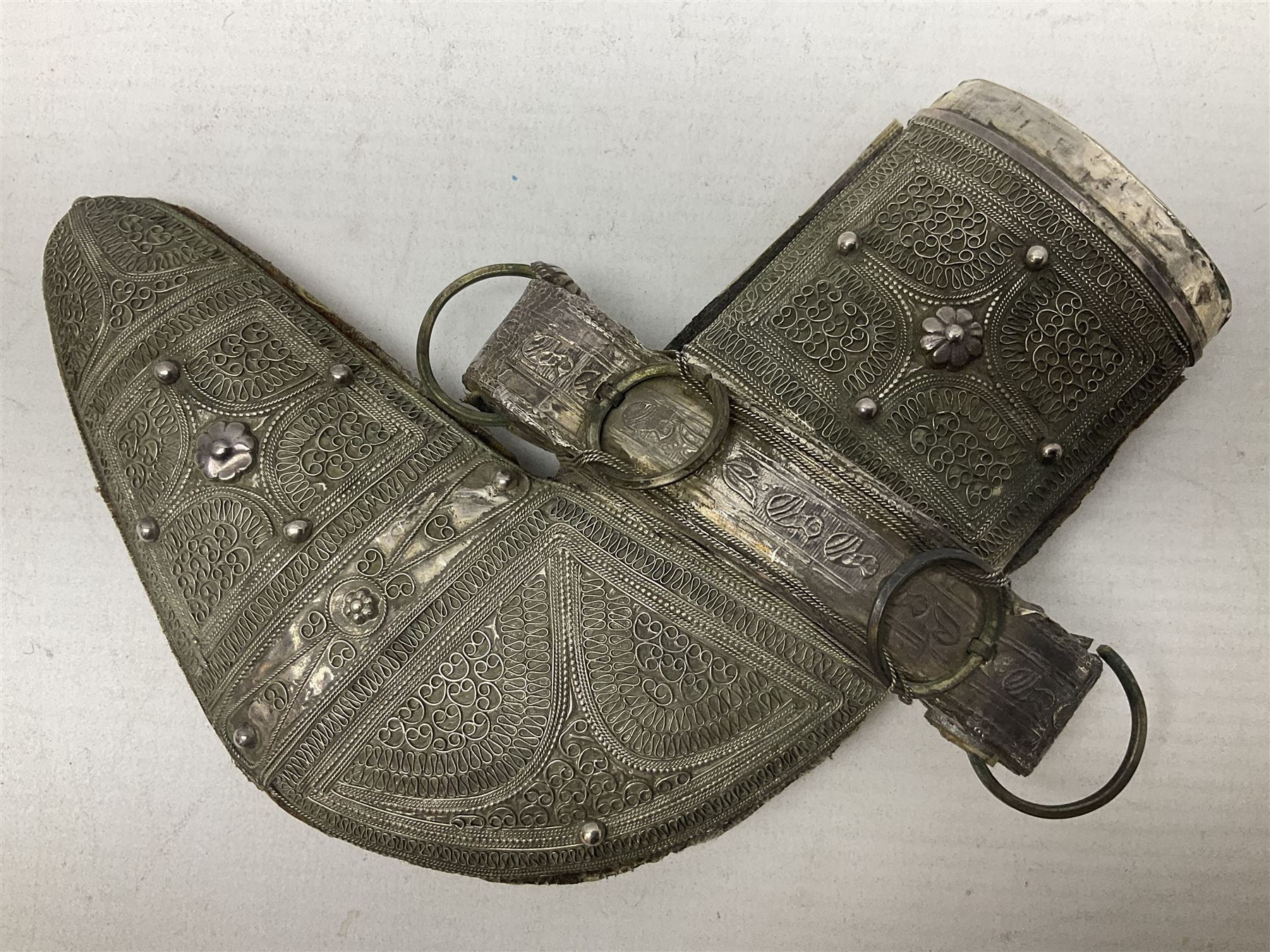 Omani Khanjar dagger, the 12.5cm curved blade with pronounced medial rib to either side, waisted horn style hilt with dome shaped pommel and inlaid pique work; in an intricately filigree decorated white metal scabbard with rings woven into the belt mount L25cm overall