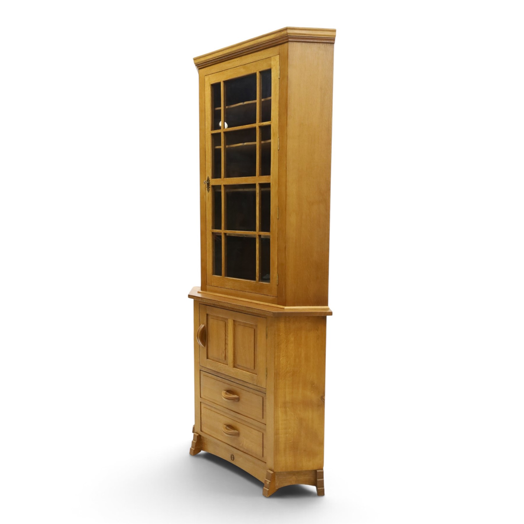 Acorn Industries - oak floor-standing corner cabinet, the top fitted with astragal glazed door enclosing four shaped shelves, the base with single panelled cupboard over two drawers, raised on four stepped feet, carved with acorn signature to top and base, by Alan Grainger, Brandsby