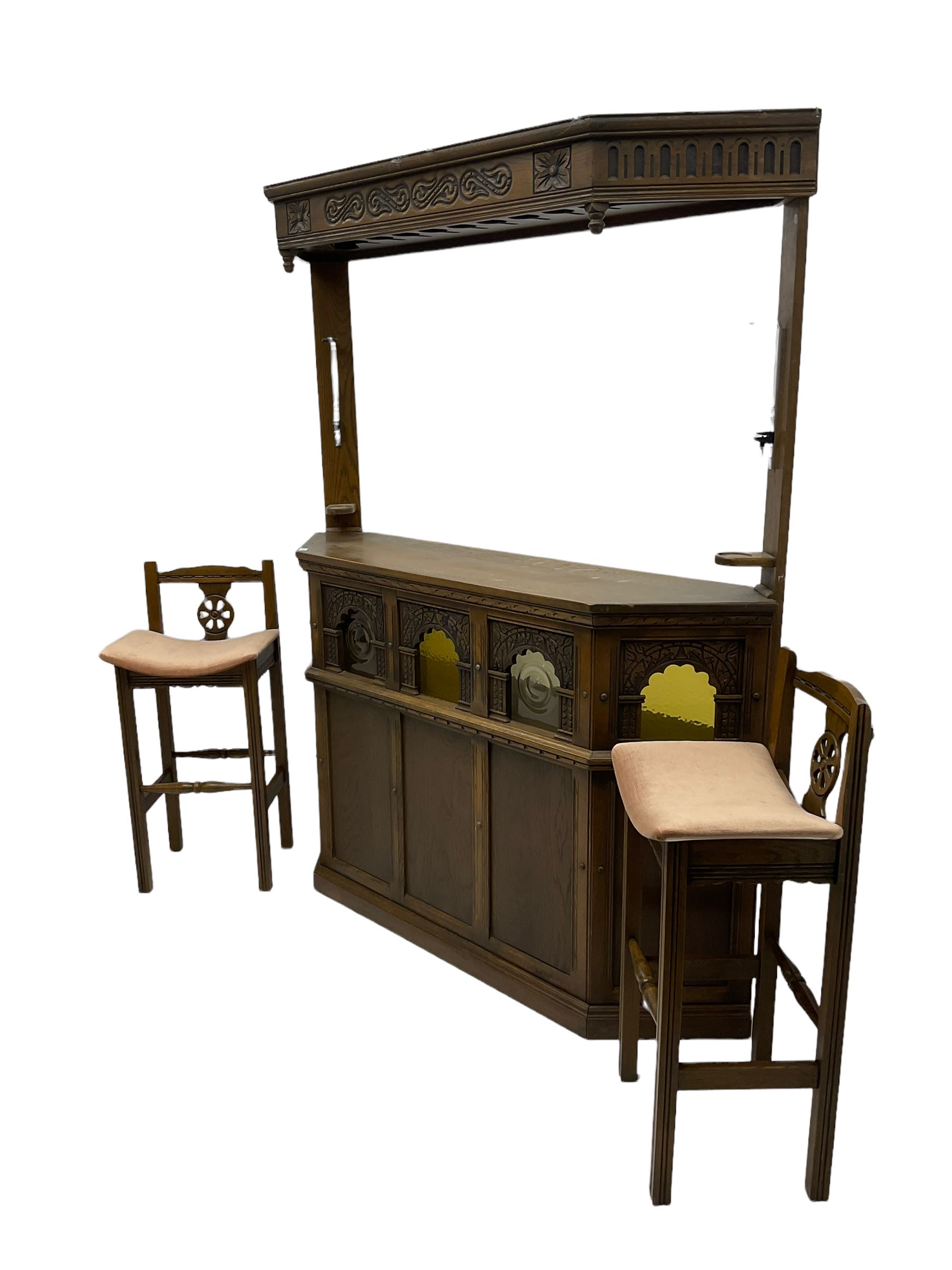 Old Charm - oak corner bar, the canopy frieze carved with scrolls, front decorated with arched apertures glazed with bullseye and mottled glass panes, skirted base, together with two bar stools