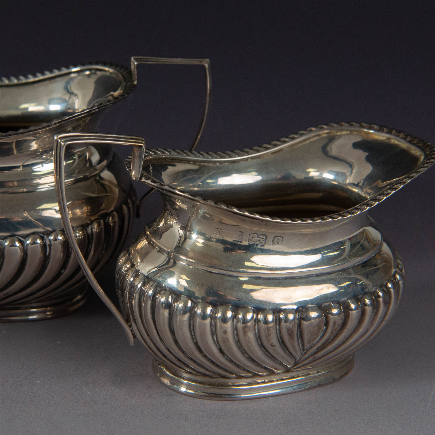 Victorian silver bachelors teapot, of part fluted oval form with ebonised wooden handle and finial, hallmarked Thomas Bradbury & Sons, London 1896, together with a Edwardian silver milk jug and open sucrier, of similar form with oblique gadrooned rims, hallmarked George Unite, Birmingham 1902 & 1906