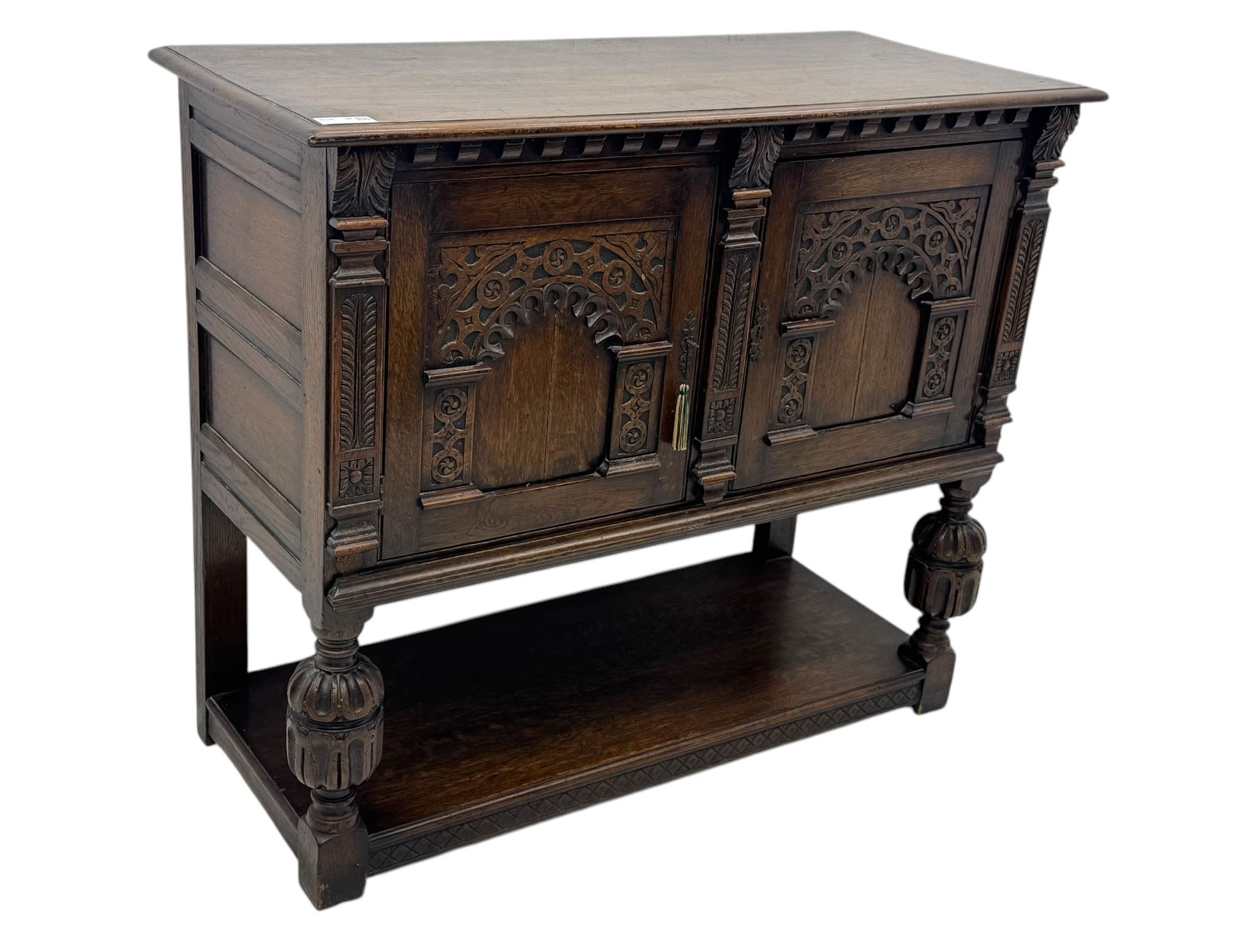 Jacobean design carved oak two door cupboard, the frieze and twin cupboard doors carved with arcaded panels and stylised foliage, raised on baluster supports united by an undertier