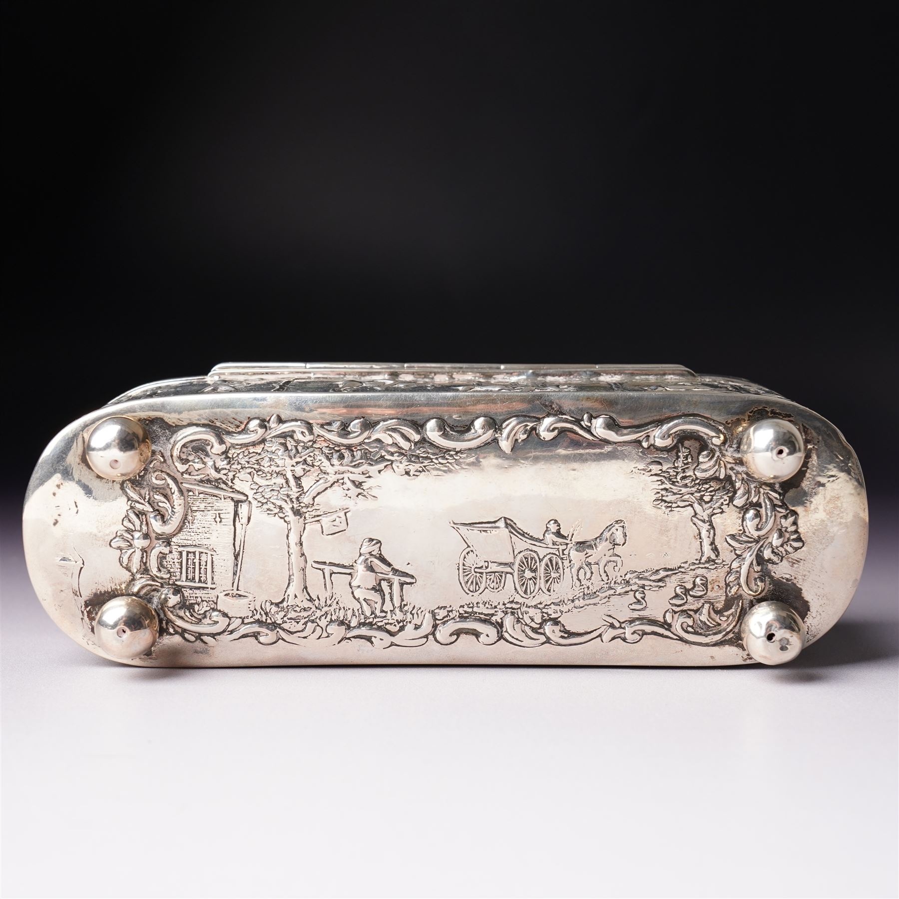 19th century continental silver box of oval design , the hinged cover with swing handle embossed with sailing ships, castle etc, the base decorated with horse and cart in rural landscape and the sides with a hunting scene on ball feet L15cm