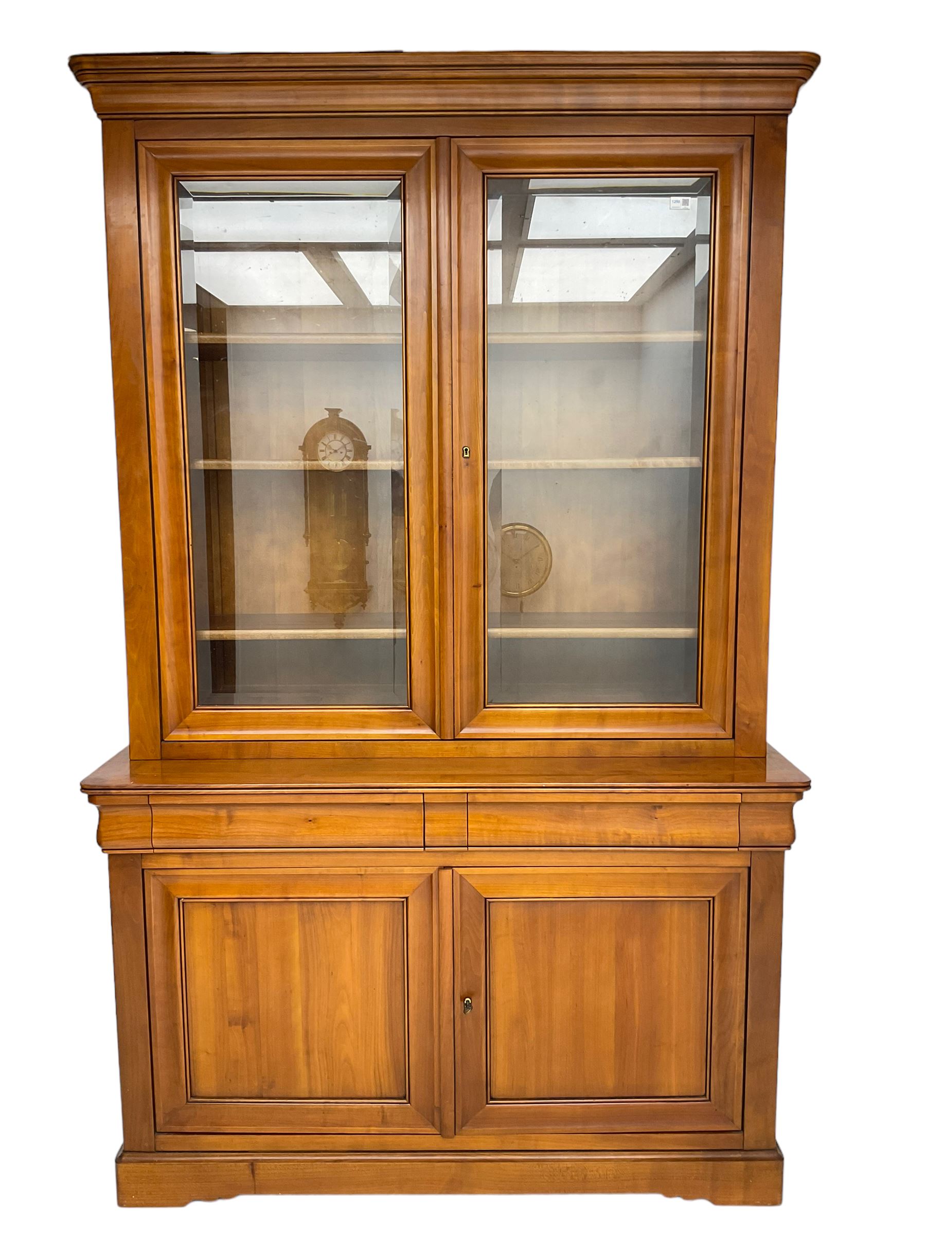 French cherry wood bookcase on cupboard, projecting cornice over two cupboard doors with bevelled glass panels enclosing three adjustable shelves, base fitted with two cushion drawers over double cupboard