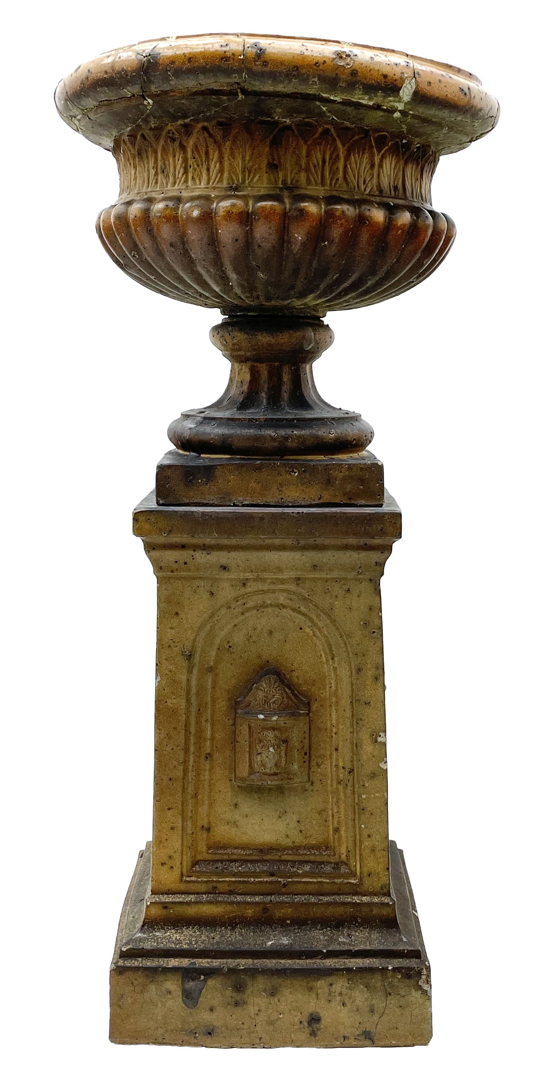 Victorian salt glazed terracotta garden urn on plinth, the Campana shaped urn with foliate decoration over gadrooned underbelly, the plinth of square tapering form, each side with recessed moulded archway decorated with urn cartouches, stepped and moulded skirt base