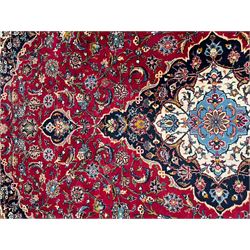 Persian Kashan crimson ground carpet, the central pole medallion decorated with flower heads, surrounded by trailing leafy branches and palmettes, scrolling border decorated with further palmettes, within floral pattern guard stripes 