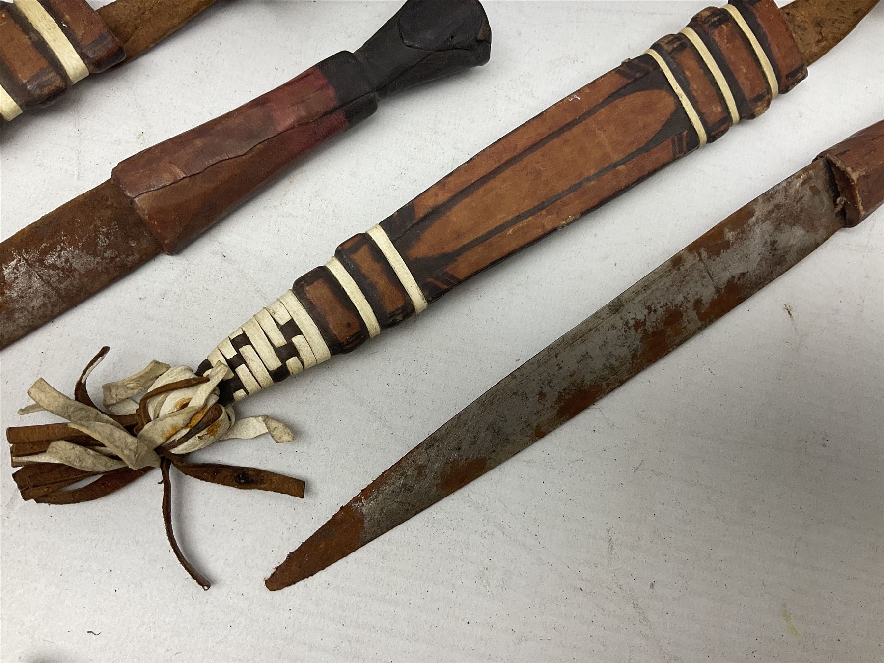Indian kukri with 29cm curving steel blade and nickel mounted horn grip; in leather covered scabbard with one skinning knife L42cm overall; Hitler Youth knife with scabbard in relic condition; and three African graduated knives each with crudely carved wooden grips and painted leather covered scabbards (5)