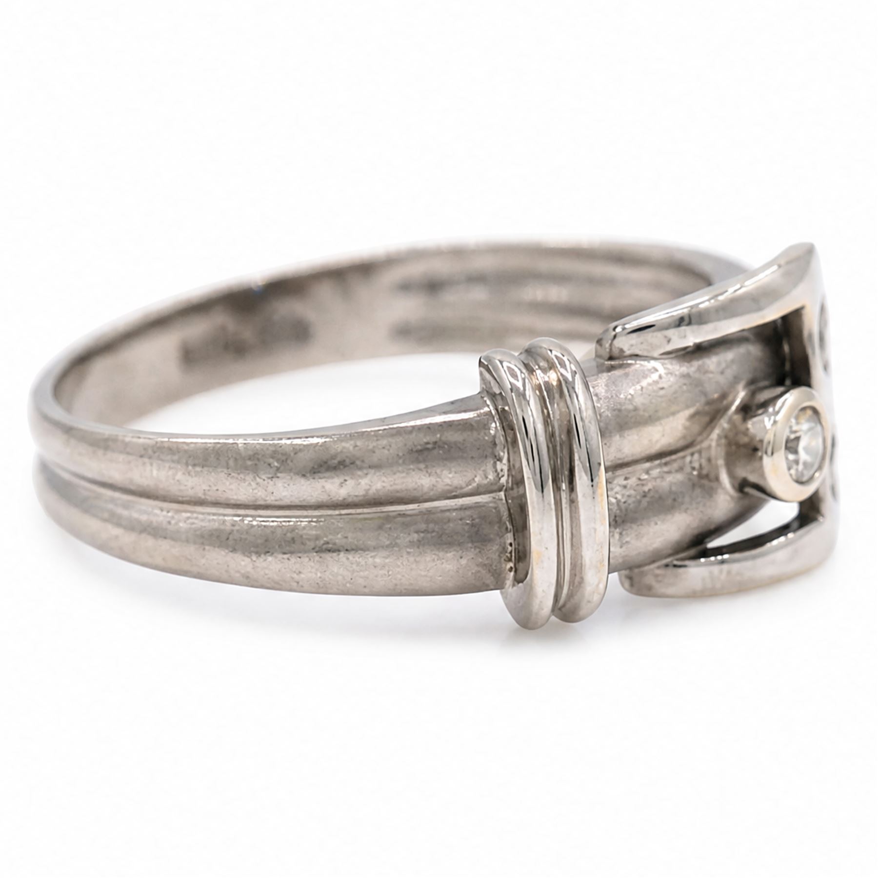 14ct white gold three stone diamond buckle ring, bezel and rubover set with three round brilliant cut diamonds, to a brushed and polished gold band, stamped 585