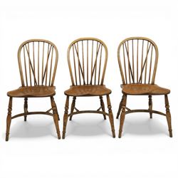 Traditional elm and beech Windsor dining chairs, each with hoop back and turned spindles over a shaped solid seat fitted with loose floral upholstered cushions, raised on turned tapering supports united by crinoline stretchers