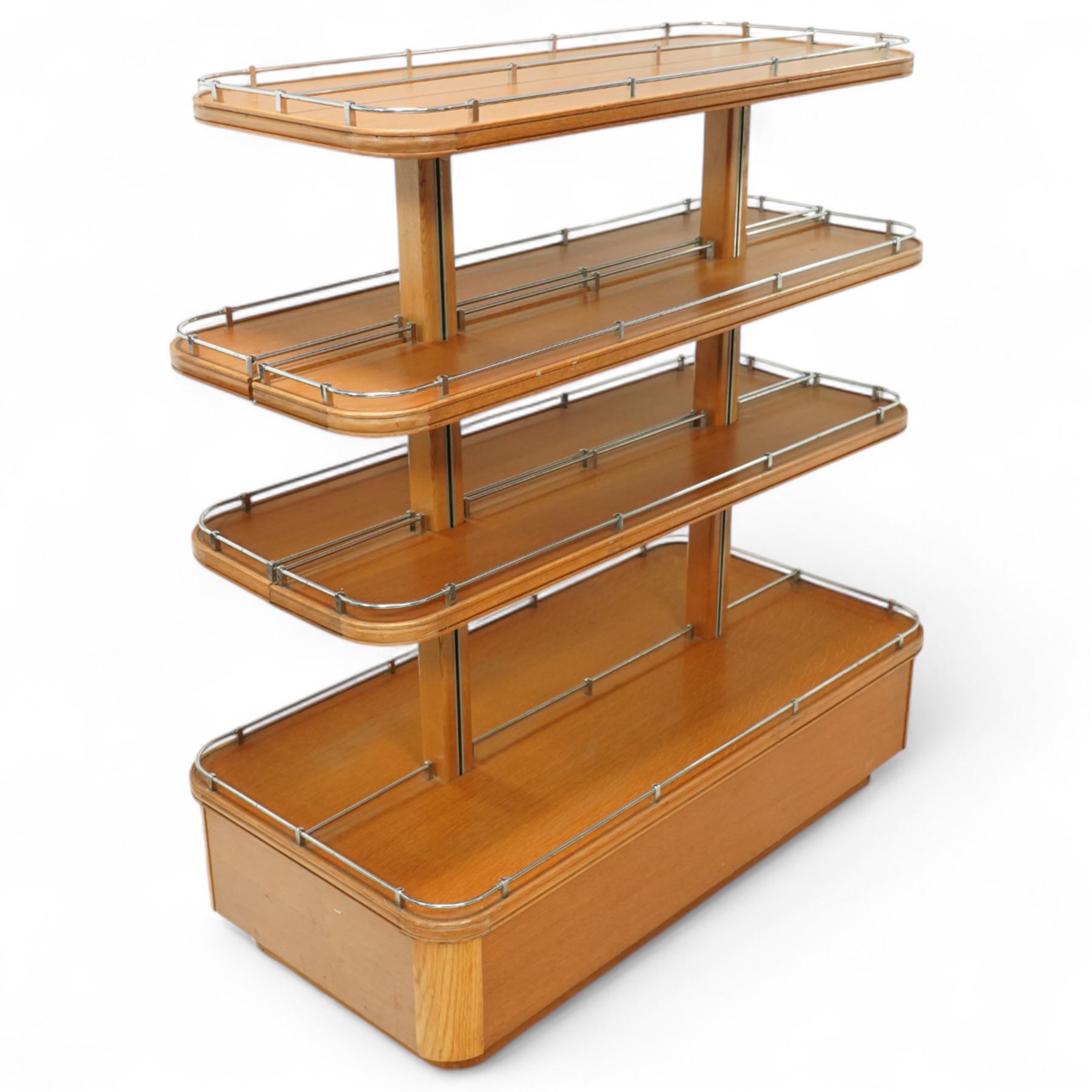 Mid-20th century retail display stand, of stepped rectangular tiered form with four graduated adjustable shelves, each with rounded corners and fitted with tubular chrome safety rails, supported by central chrome-mounted wooden uprights over a plinth base
