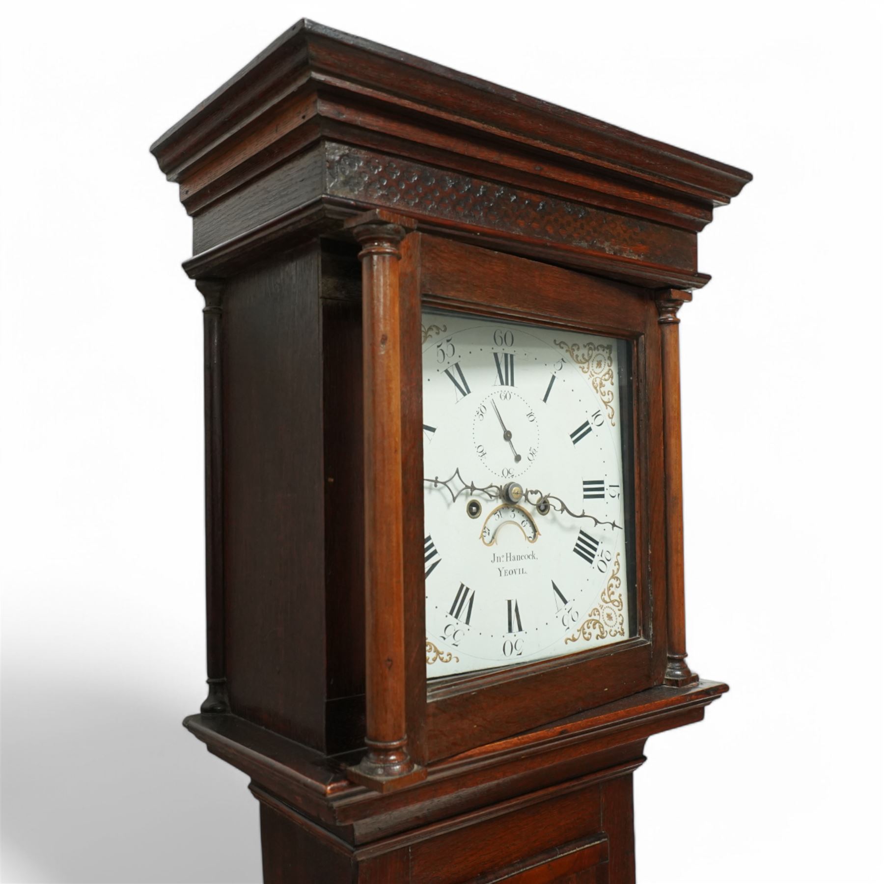 John Hancock of Yeovil (Sommerset) - oak cased 8-day longcase clock c1810, with a flat topped pediment, blind frieze and broad cornice, square hood door with attached wooden pilasters and capitals, long trunk door on a square plinth with applied skirting, painted dial with steel hands, gilt painted spandrels, Roman numerals, minute track and five-minute Arabic's, with seconds dial and date aperture, dial pinned via a falseplate to a rack striking movement, striking the hours on a bell. With weights and pendulum.