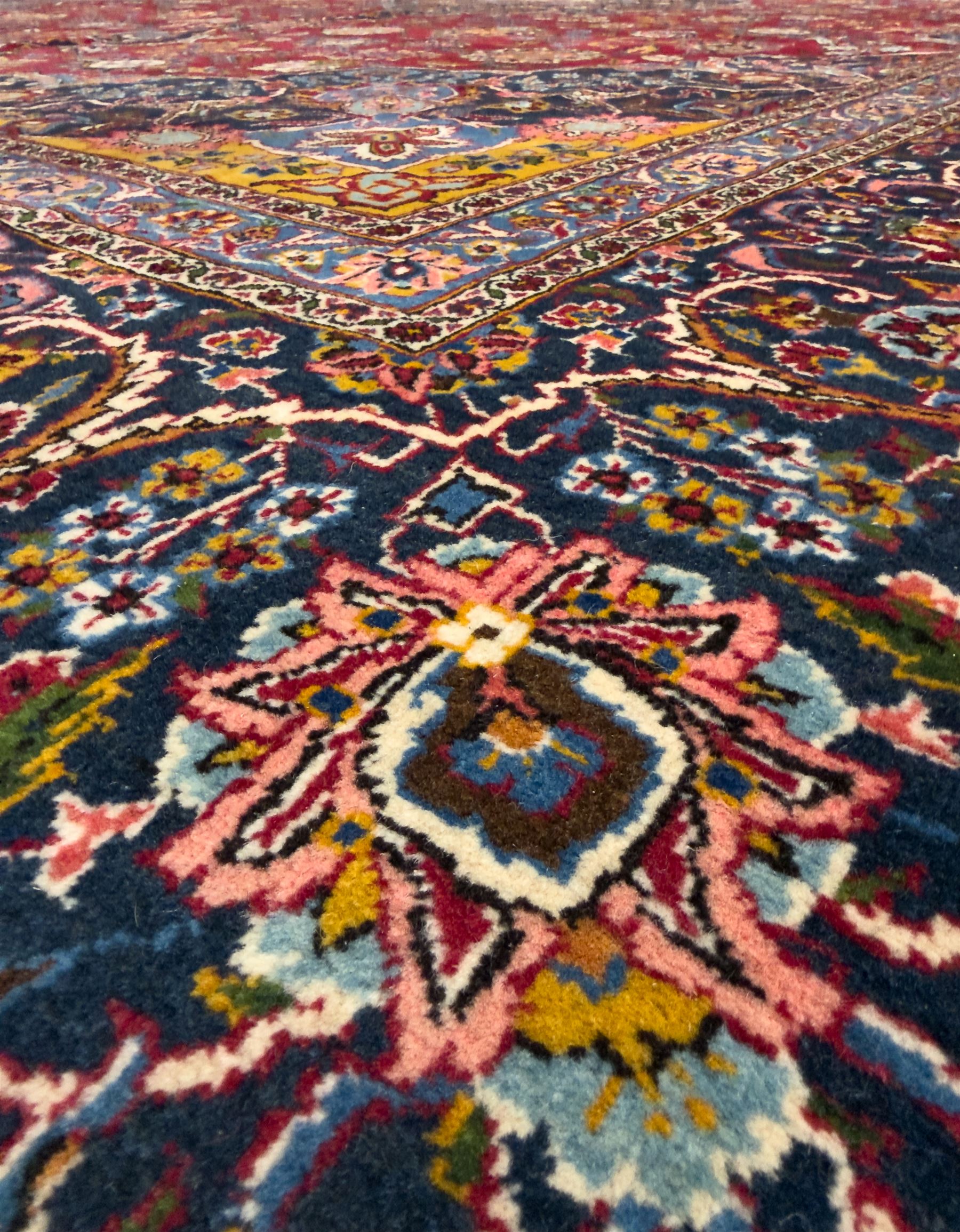 Central Persian Kashan hand-knotted carpet, madder red field with an intricate design of scrolling vines, palmettes, and rosettes with a central lobbed medallion with pendant motifs in shades of blue and ivory, and spandrels all within a blue-ground border of palmettes and flowerheads between multiple guard borders, 450cm x 335cm 