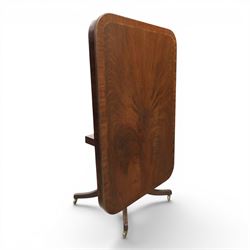 Regency mahogany tilt-top dining table, crossbanded rounded rectangular top, raised on a splayed base, terminating in brass castors
