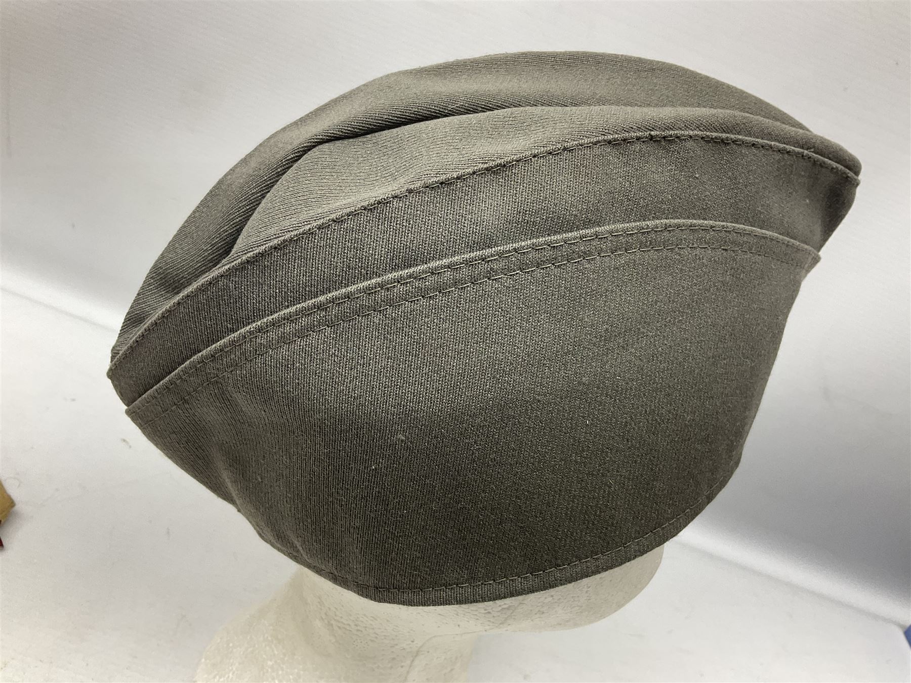 Four side caps - WW2 Russian, post-WW2 Russian and two East German; all with badges, one with multiple metal badges (4)