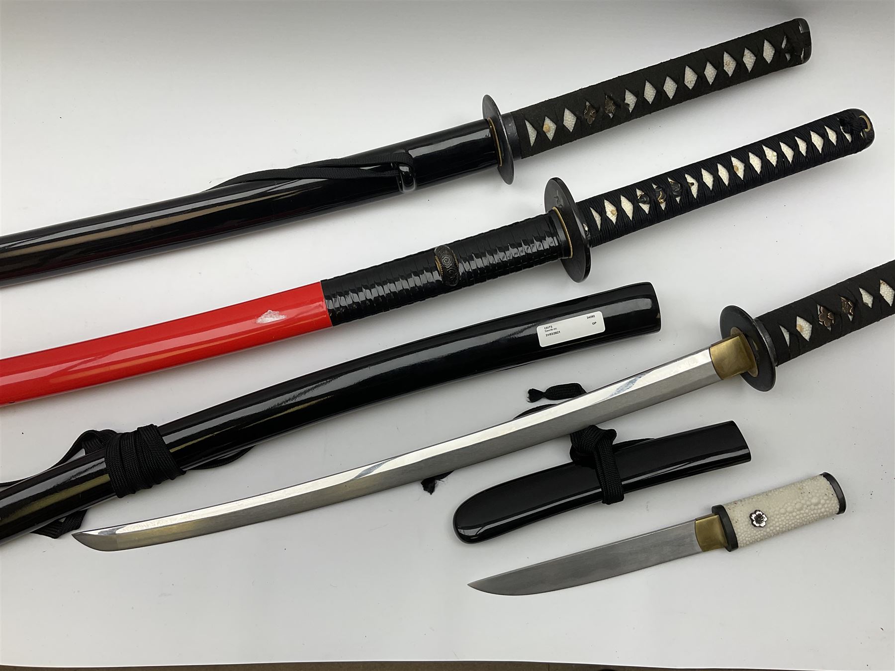 Reproduction Japanese sword daisho of katana and wakisashi with matching tanto; together with another reproduction katana; all with simulated fish skin grip and lacquered saya (4)