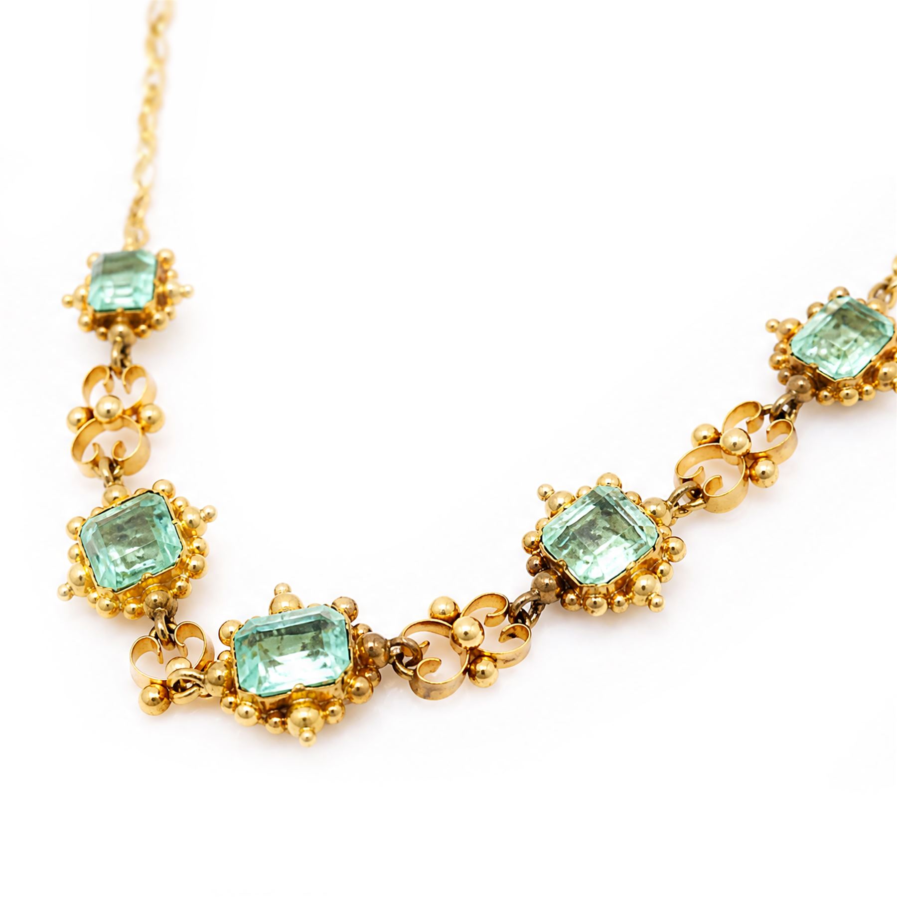 19th century gold emerald necklace, seven closed back octagonal cut and square cut emeralds, surrounded by a fancy bead setting, each spaced by a pierced scroll and bead design link, to a cable link chain necklace, with The Gem & Pearl Laboratory report