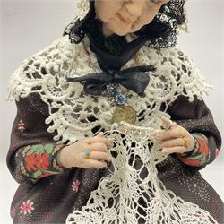 Anna Meszaros Hungary - hand made needlework figurine 'Old Lady' seated on a stool wearing a lace trimmed black/white/red floral full length dress and hat, working on a piece of lace H30cm  Auctioneer's Note: Anna Meszaros came to England from her native Hungary in 1959 to marry an English businessman she met while demonstrating her art at the 1958 Brussels Exhibition. Shortly before she left for England she was awarded the title of Folk Artist Master by the Hungarian Government. Anna was a gifted painter of mainly portraits and sculptress before starting to make her figurines which are completely hand made and unique, each with a character and expression of its own. The hands, feet and face are sculptured by layering the material and pulling the features into place with needle and thread. She died in Hull in 1998.