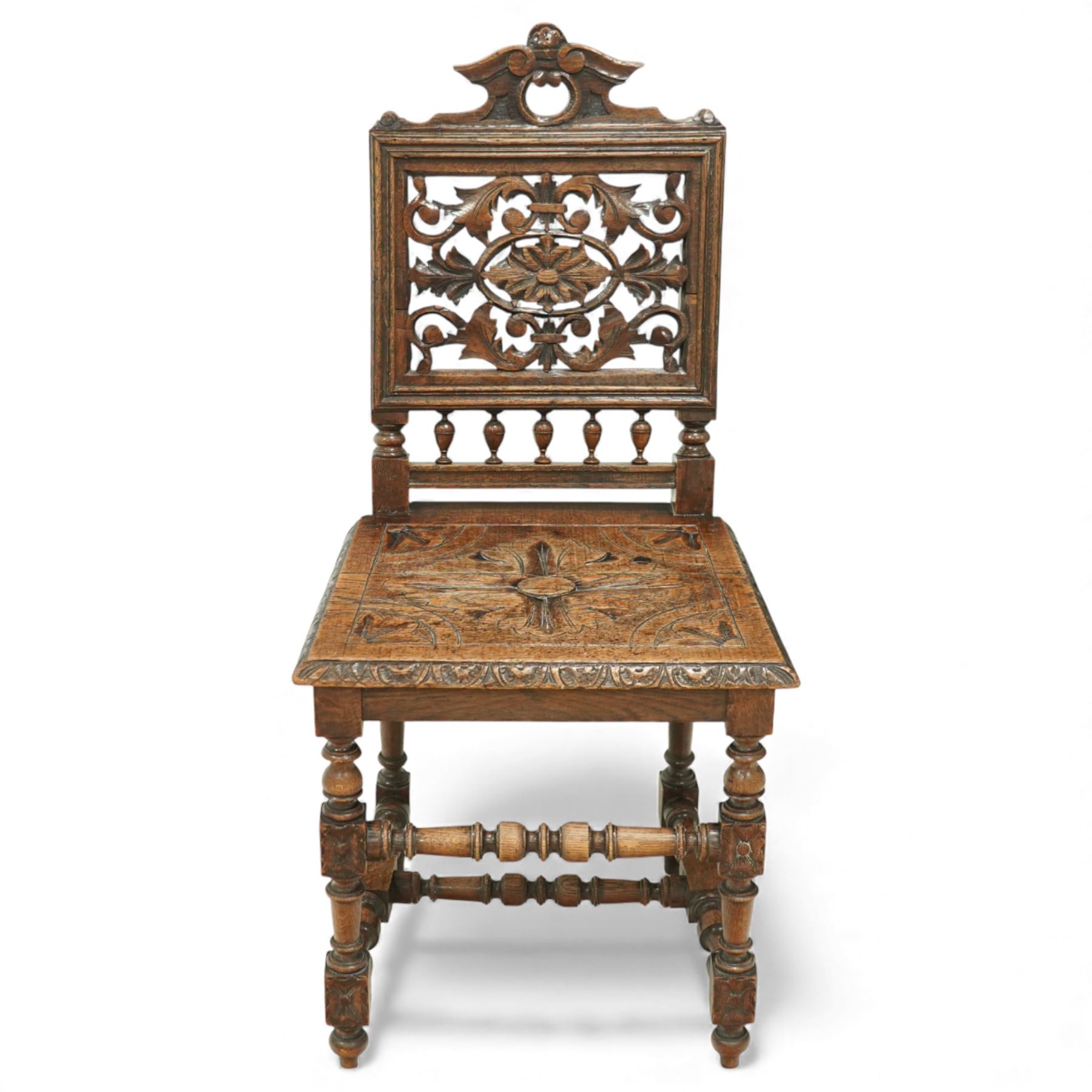 18th century carved oak hall chair, the rectangular pierced back carved with scrolling foliate ornament and central rosette beneath a shaped cresting, the boarded seat carved with stylised foliage, raised on turned legs united by stretchers