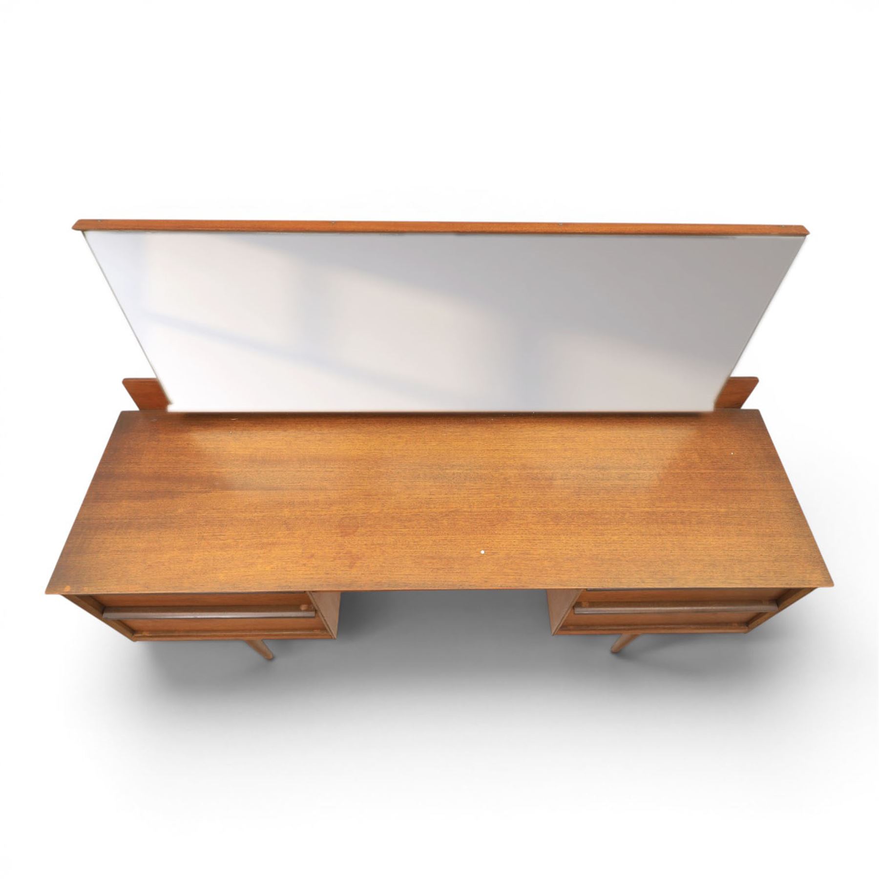 Austinsuite - mid 20th century teak headboard with bedside cabinets and matching  mirrored dressing table, the headboard with floating single drawer bedsides raised on a single tapering support, the dressing table with attached tilting mirror, above rectangular top with kneehole and two banks of two drawers, raised on tapering supports

Headboard H 84cm, D 40cm, W 229cm, W between bedsides 151cm 
Dressing table H 113cm D 44cm, W 149cm, H to underside of dresser 61cm