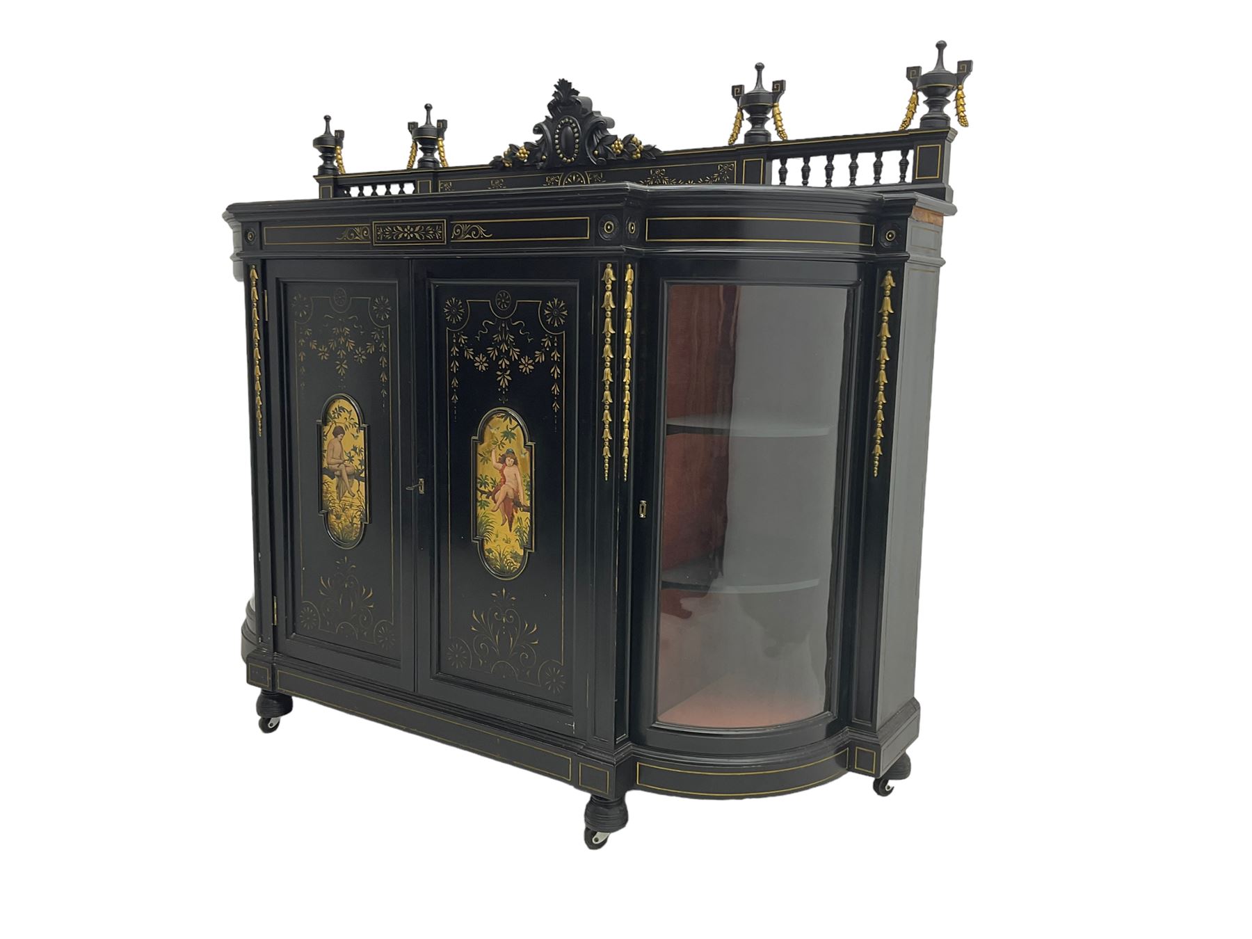 Victorian ebonised credenza side cabinet, raised balustrade back with urn finials and a central carved cartouche, carved and gilded with floral garland decoration, central doors with gilt panels painted with figures sitting over a lake enclosing two shelves, flanked by applied bellflower detail and glazed bow-front side doors, raised on ring turned feet with castors