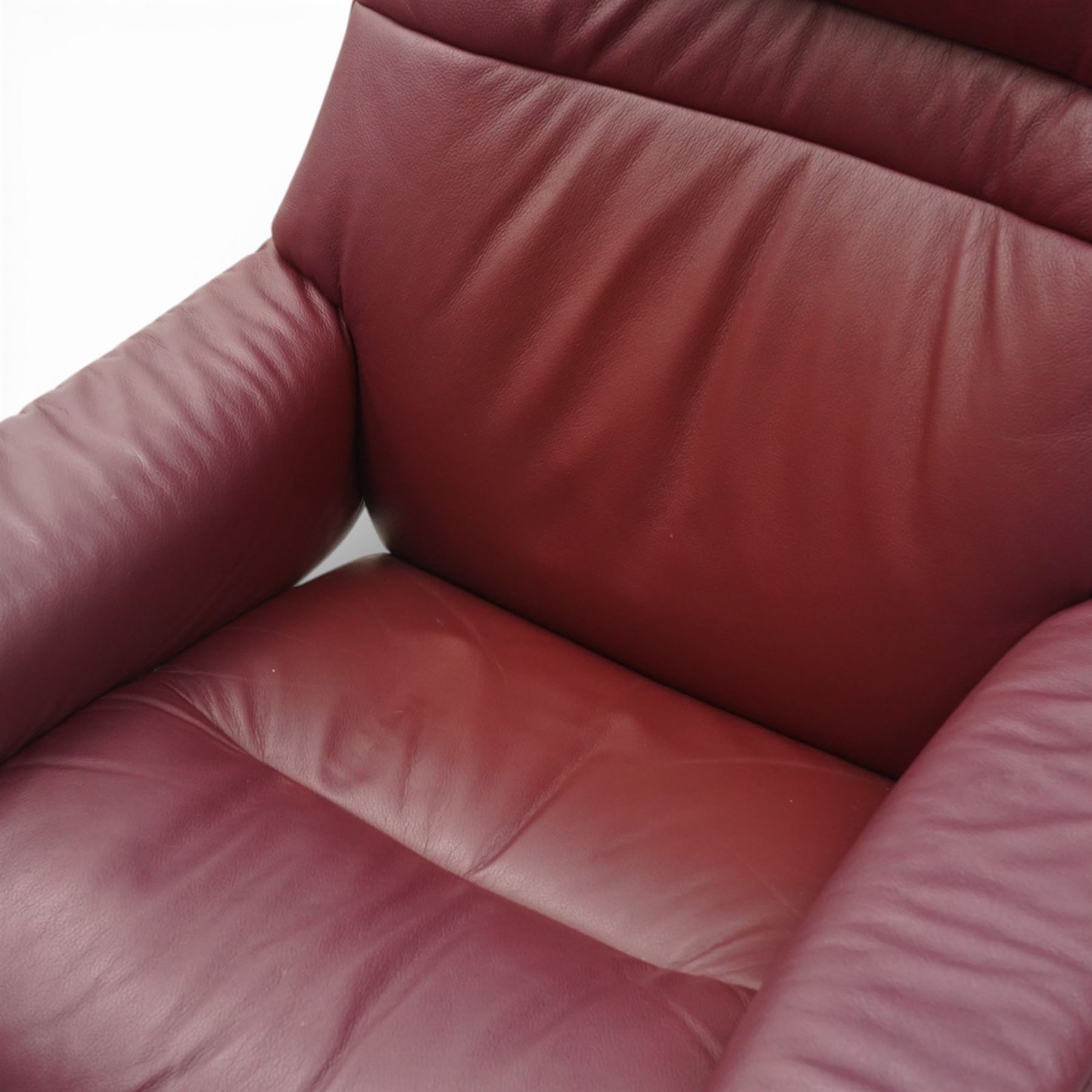 Ekornes - Stressless reclining armchair and matching footstool, upholstered in oxblood leather with padded headrest and segmented back cushion, shaped armrests with exposed adjustment handles, raised on stained laminated beech circular swivel base, the conforming stool on matching ring base