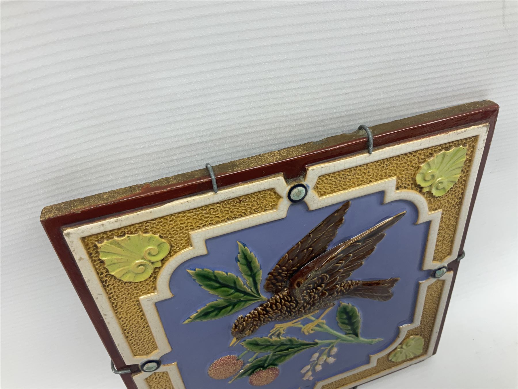 19th century Minton & Co majolica tile, decorated in relief with a bird upon a fruiting branch against a blue ground, with textured ochre border and anthemion to each corner, impressed mark verso, H19.7cm