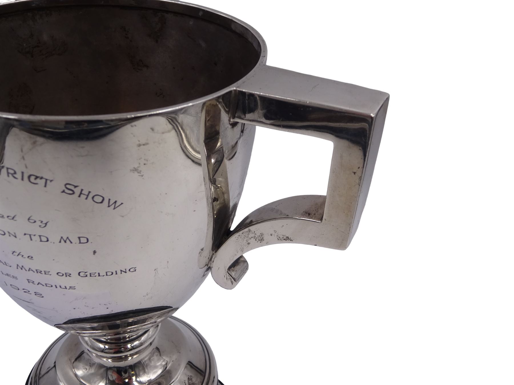 1920s silver trophy cup, with angular twin handles, upon knopped stem with circular spreading foot, the body with presentation engraving 'Burniston & District Show, presented by S Fox Linton TD MD, for the Best Agricultural Mare or Gelding, 10 miles radius, 1928' and engraved with winners verso, hallmarked Charles Boyton & Son 1921, upon black plastic base, including base 25cm