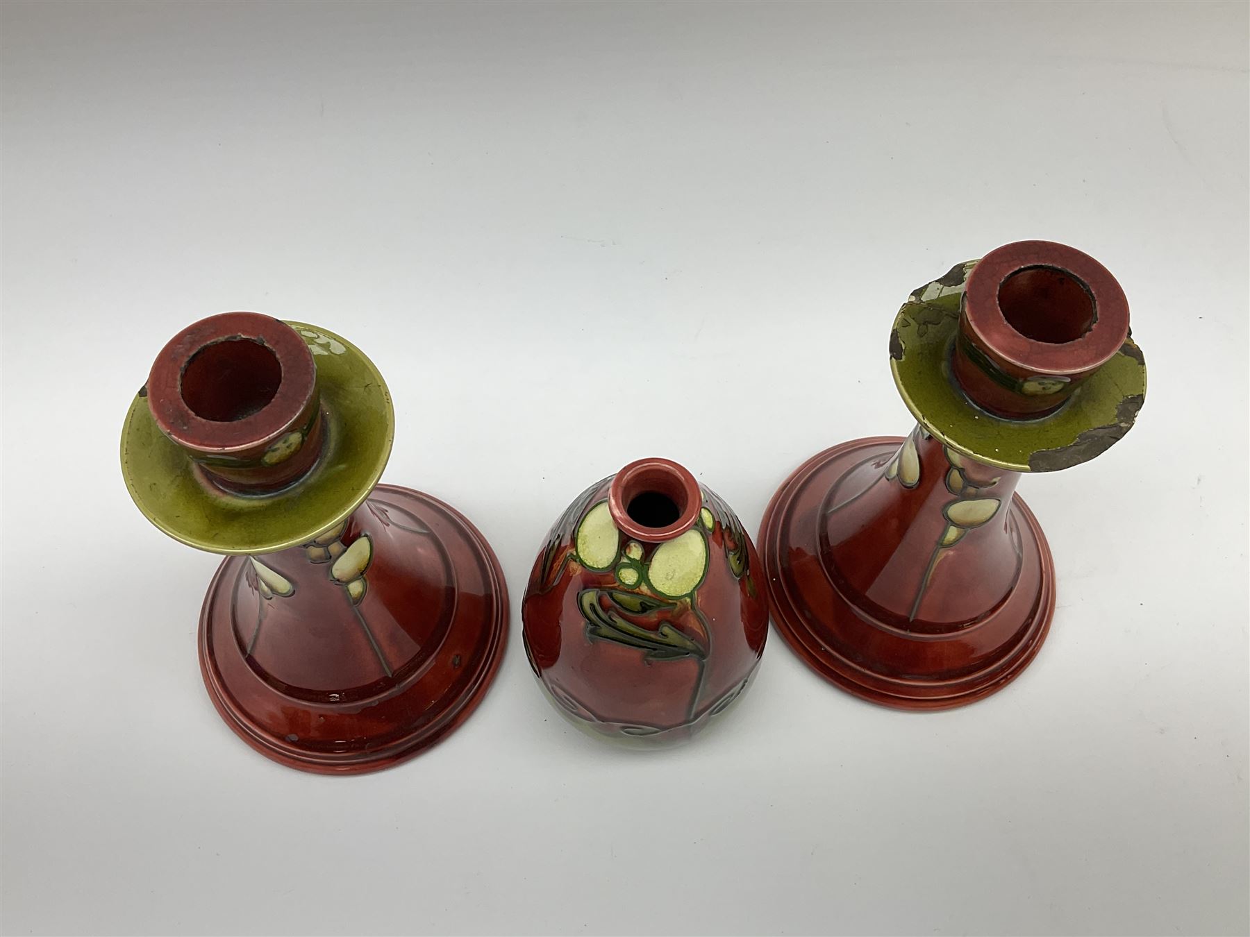 Minton Secessionist vase, with tube-lined stylised flower head decoration upon a red and green ground, printed mark to base 'Minton Ltd, No. 31', together with a matching pair of Minton Secessionist candle sticks, candlestick H17cm
