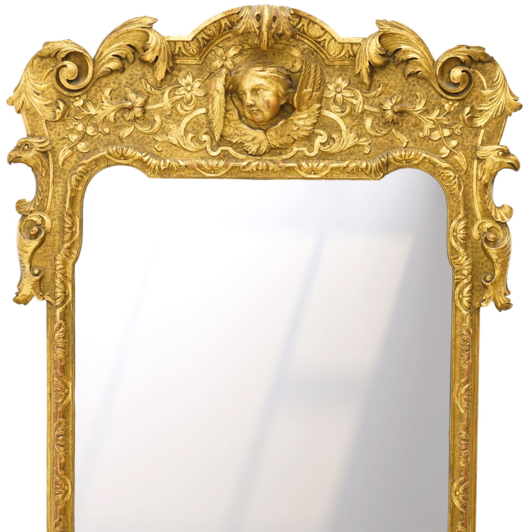 In the manner of Thomas Johnson - circa 1900 Georgian Revival giltwood wall mirror, the shaped rectangular plate within a foliate and scallop carved slip and richly ornamented frame, surmounted by a pierced cartouche crest centred with a protruding relief carved winged cherub mask and issuing scrolling acanthus and floral ornament, the sides with eagle masks over acanthus scrolls, terminating in a shaped apron with moulded rosette and spiralling acanthus leaves