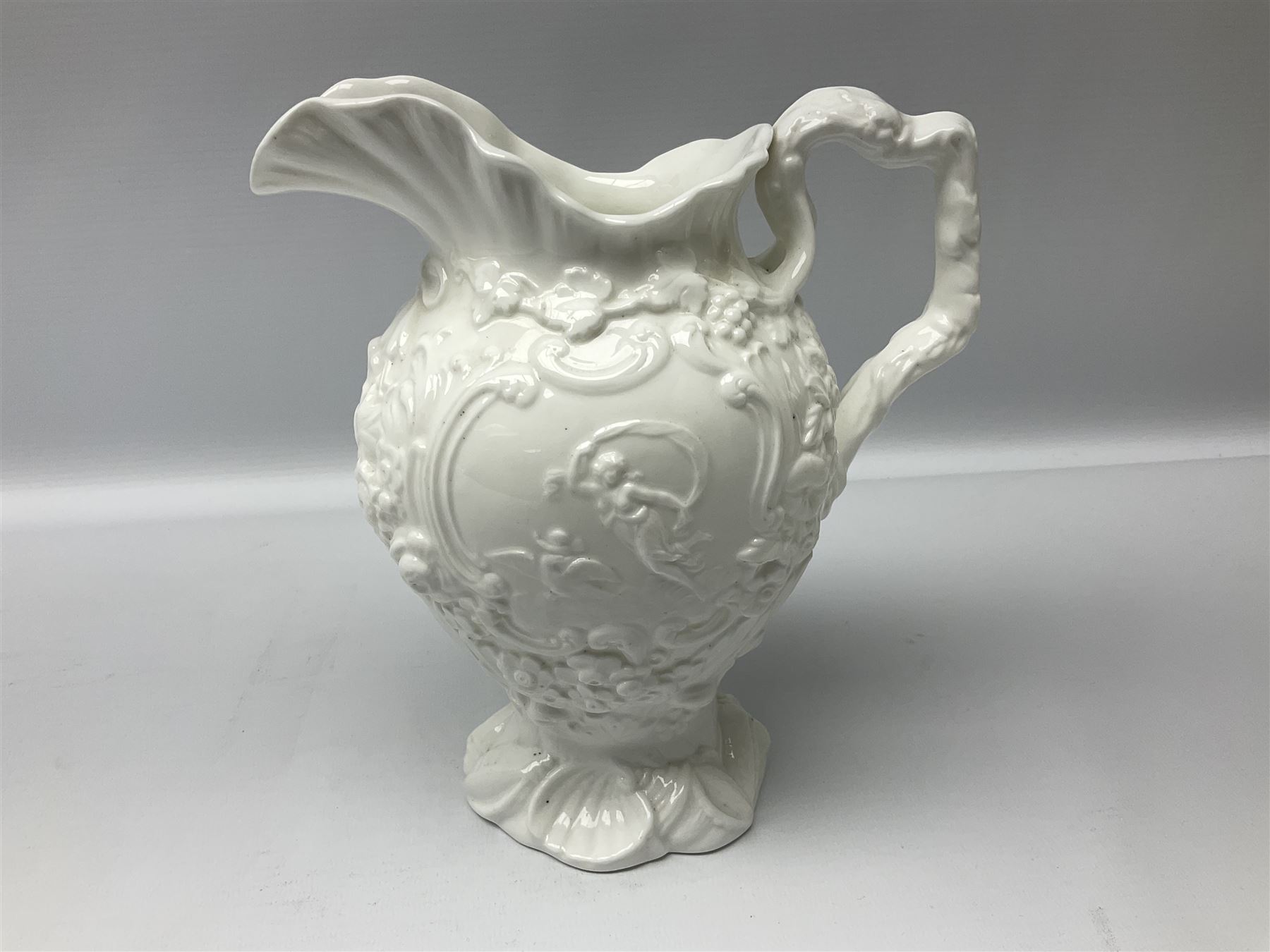 Pair of early/mid 19th century Copeland and Garrett white glazed pitchers, modelled in the Georgian style and moulded with the figures of Venus the Roman Goddess of Love, and Aurora the Roman Goddess of Dawn, within C scroll borders and foliate surround, the naturalistically modelled handle leading to a fruiting vine beneath the rim, upon a spreading base moulded with seashells, with printed green crowned wreath mark beneath, H20cm