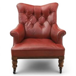 Early 20th century style oxblood red leather Chesterfield armchair, deep buttoned shaped back over padded scroll arms and loose seat cushion, raised on turned mahogany front supports with brass caps and castors