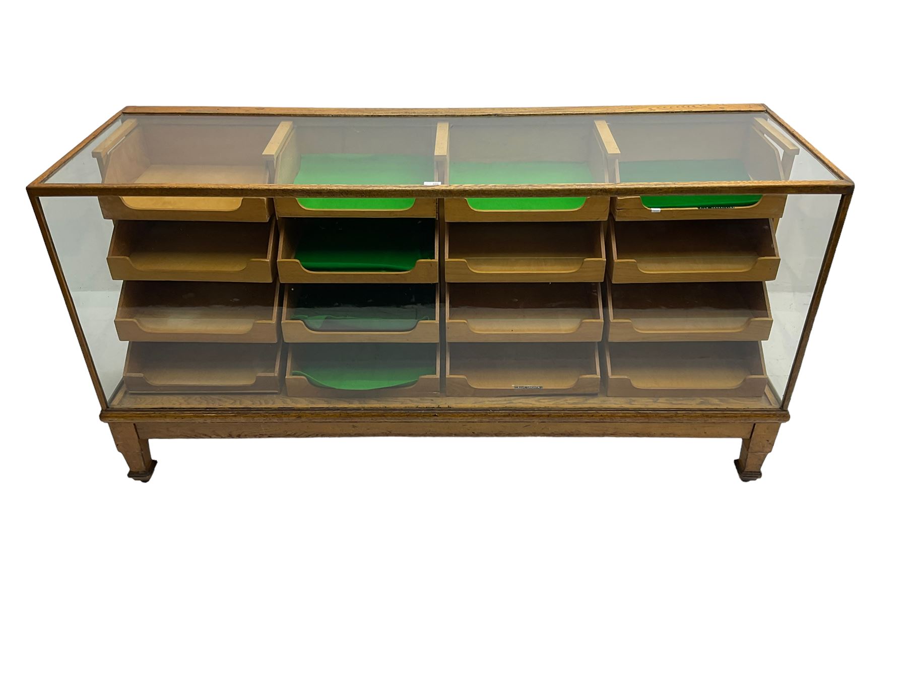 Early 20th century oak framed haberdashery shop counter, glass panel exterior enclosing sixteen graduating drawers with oak fronts and handles, raised on shaped tapering supports 