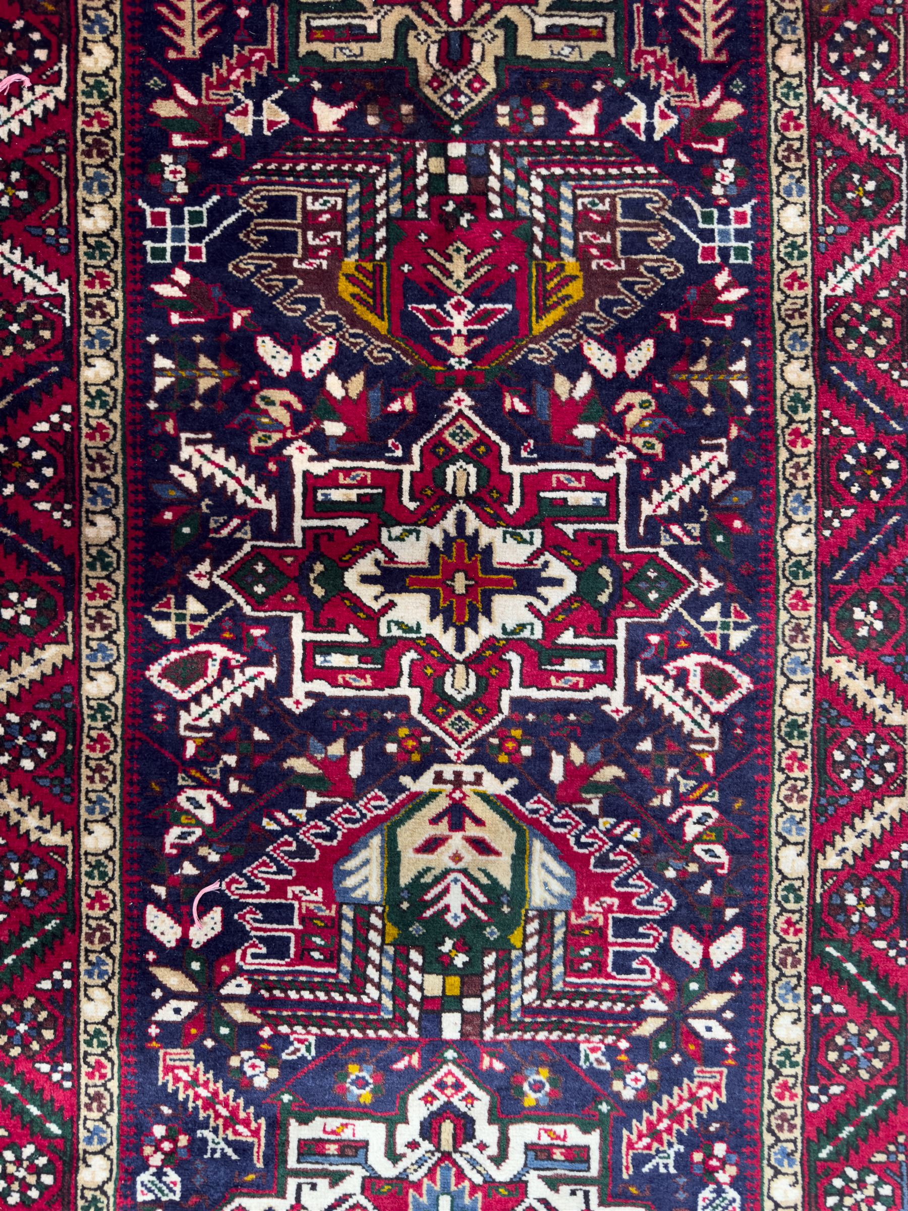 Northwestern Persian Heriz hand-knotted runner, dark indigo field with a series of linked stepped medallions in madder red, ivory, and green, flanked by angular floral motifs, within a madder red border of stylized rosettes and geometric vine motifs 405cm x 95cm