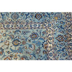 Central Persian Kashan hand-knotted carpet, pale blue field decorated with an all-over scrolling floral vine design incorporating stylized palmettes, rosettes and foliate sprays enclosed by a conforming floral vine border between multiple guard stripes, with cotton fringe ends 