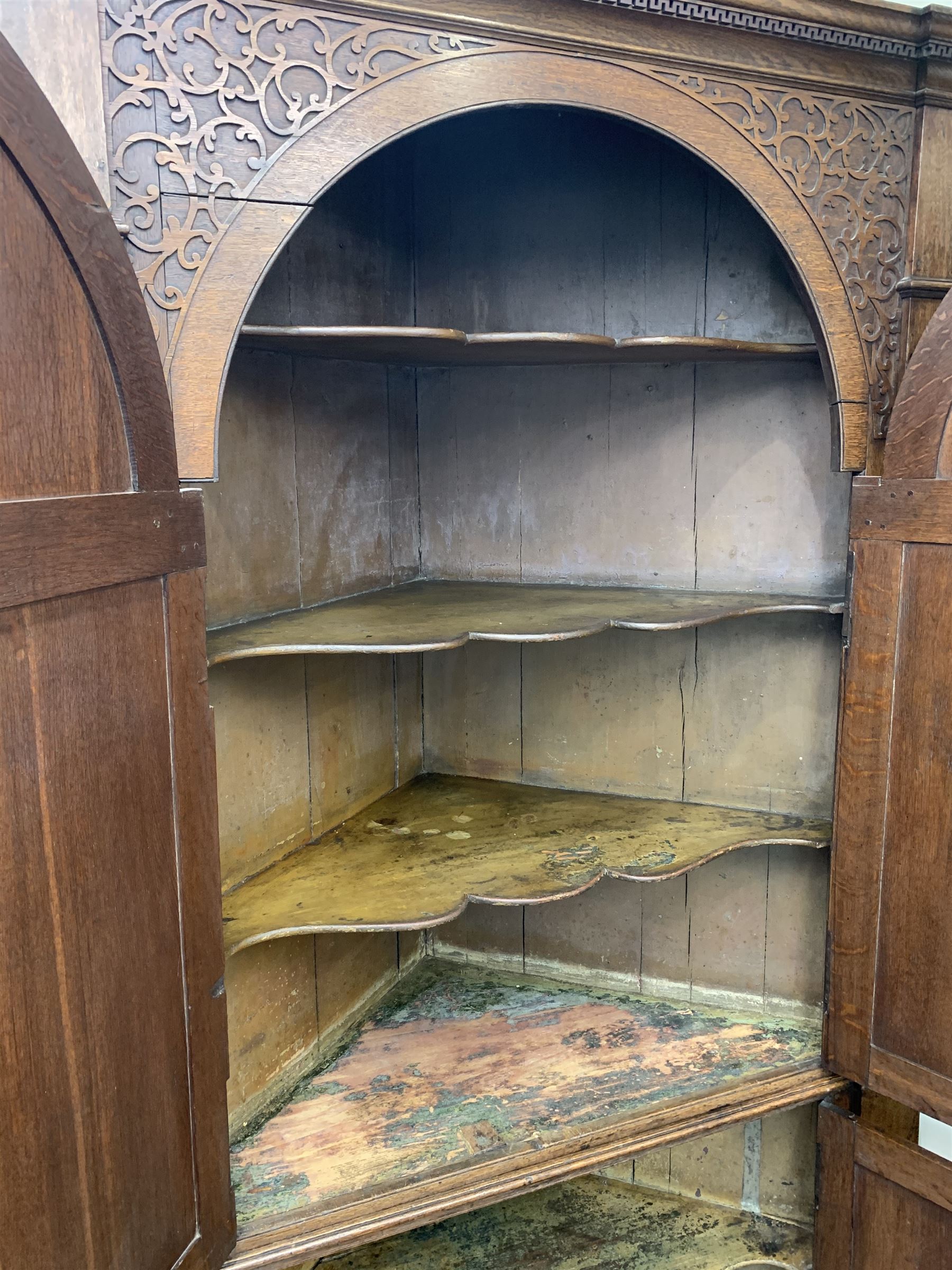 Large George III oak corner cupboard, projecting cornice over two stepped arch doors with fielded panels and blind fret work spandrels, flanked by fluted uprights, cupboard below enclosed by two fielded panel doors, the painted interior fitted with shaped shelves
 