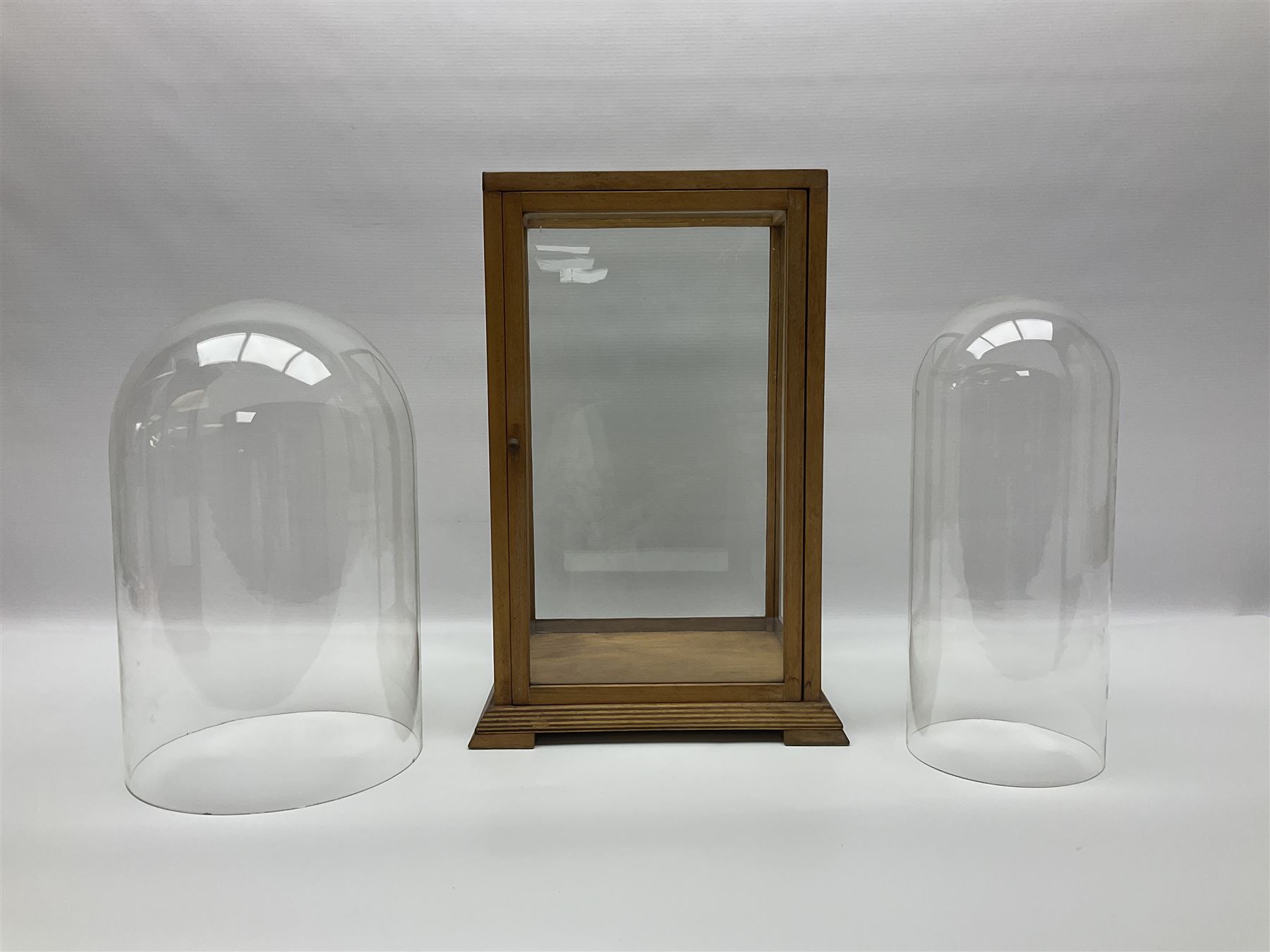 Tabletop glass display cabinet, with hinged door, together with two glass domes