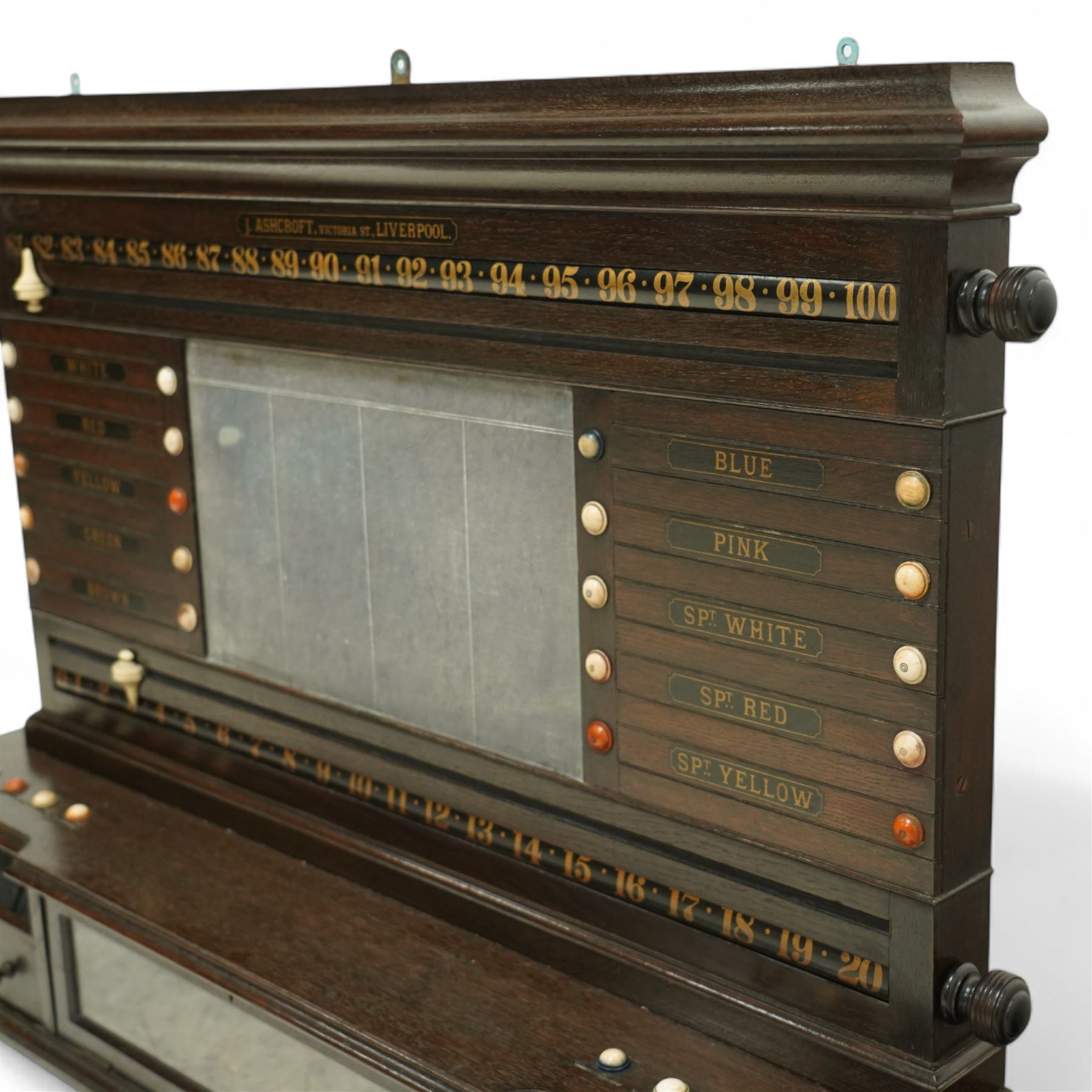 Victorian wall-mounted oak and walnut cased scoreboard,  moulded top, with a name stencilled in the frieze ‘J. Ashcroft, Victoria Street, Liverpool’, the board with chalk panel in the centre for recording scores, sliding panels on both sides for the various games of Billiards and Snooker, two numbered rotating arms with adjustable sliding score keepers, the base section with 5 apertures on each side, and coloured ivory roundels, all with glass front for viewing the tokens inside, with drawers beneath, the centre has a long glass panel for storing billiard balls, circa 1870 This item has been registered for sale under section 10 of the APHA Ivory Act Reference UNEGEBLB
