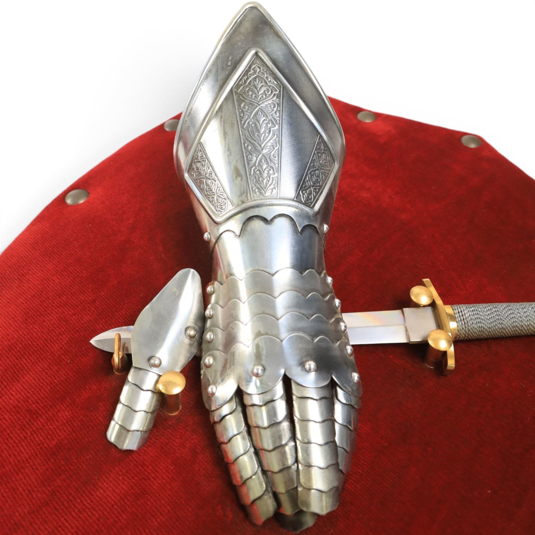 Three replica gauntlets, each housed upon a red wall shield, two with daggers, the third with a sword, largest H102cm