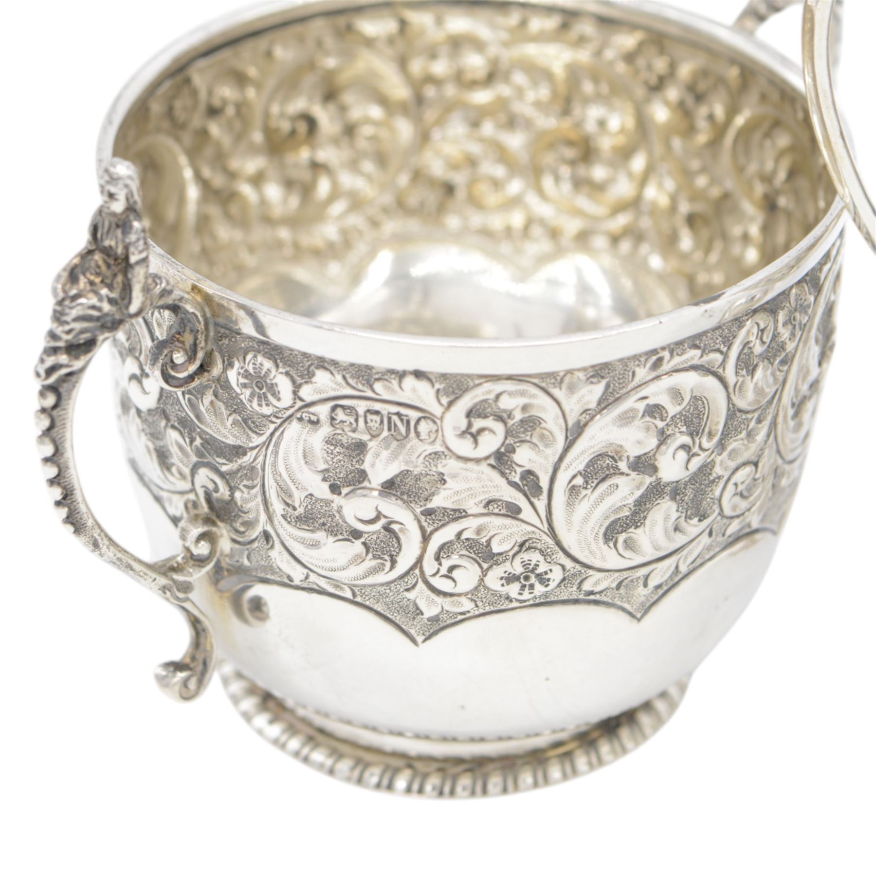 Late Victorian silver twin handled sugar bowl, profusely embossed with floral and scrolling decoration and acanthus capped handles, upon stepped oval base, hallmarked Josiah Williams & Co, London 1897, together with a Victorian twin handled sugar bowl, of circular form with embossed and chased foliate decoration and seated figures capping each handle, upon circular base, hallmarked London 1888, maker's mark indistinct, tallest H11cm