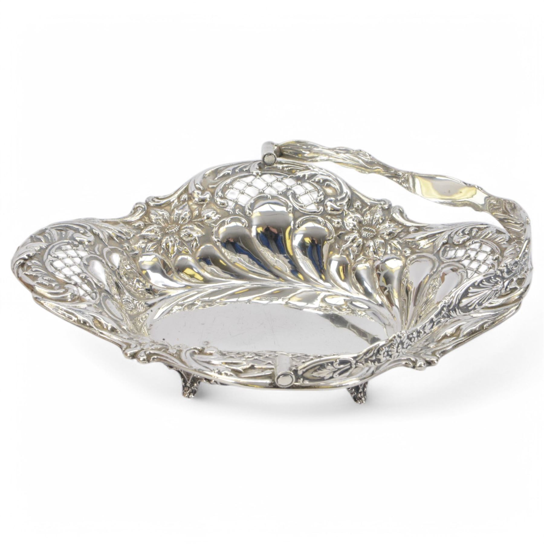 Edwardian silver swing handled basket, of oval form with shaped rim, embossed with floral decoration and with pierced latticework sides, upon four pad feet, hallmarked Chester 1905, maker's mark worn and indistinct