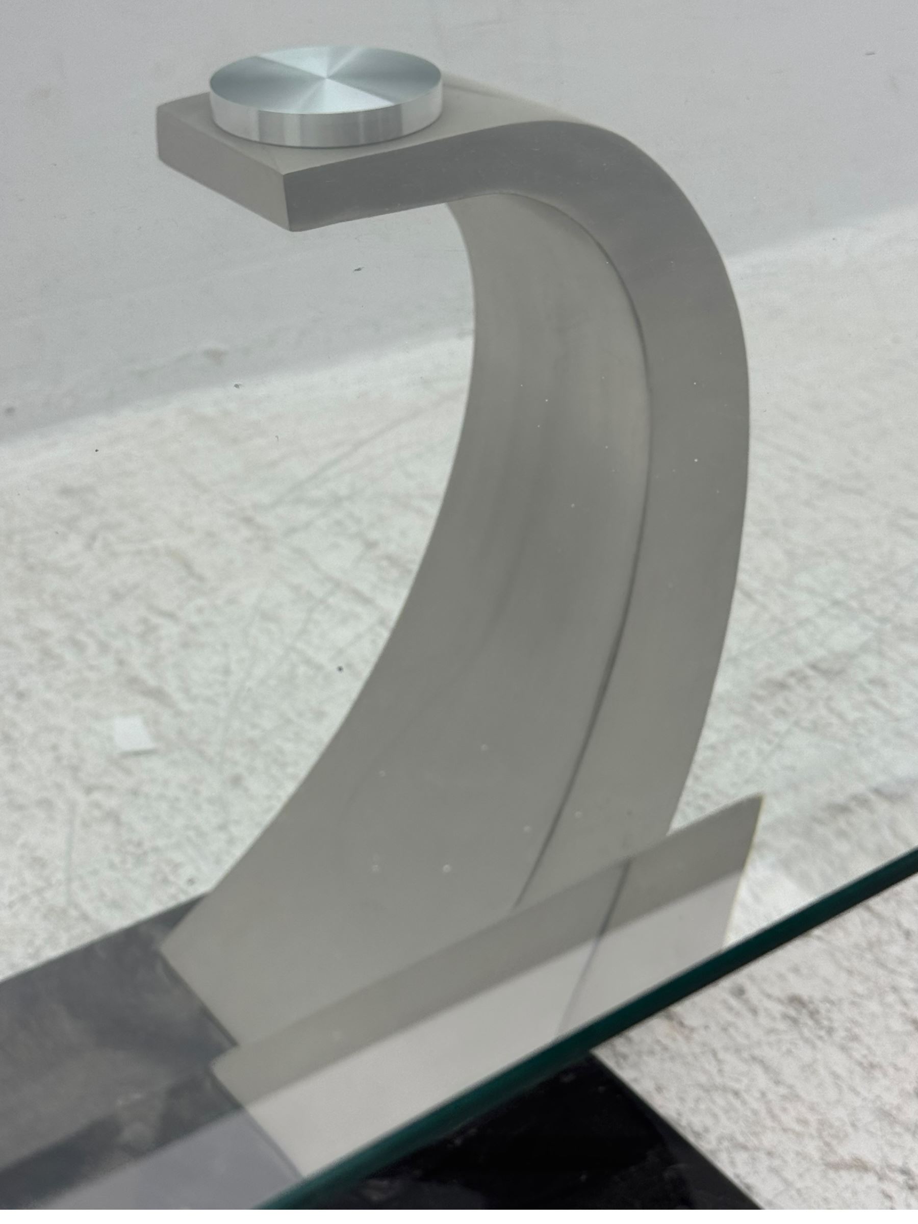 Contemporary coffee table, rectangular clear glass top over brushed stainless steel curved supports, mounted on a rectangular base