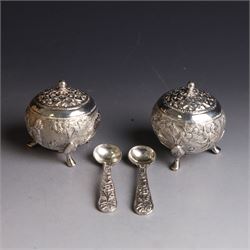 Pair of Middle Eastern silver cruets, of spherical form with pierced tops, embossed with figures, elephants and village scenes, unmarked, together with a pair of silver condiment spoons embossed with floral decoration 